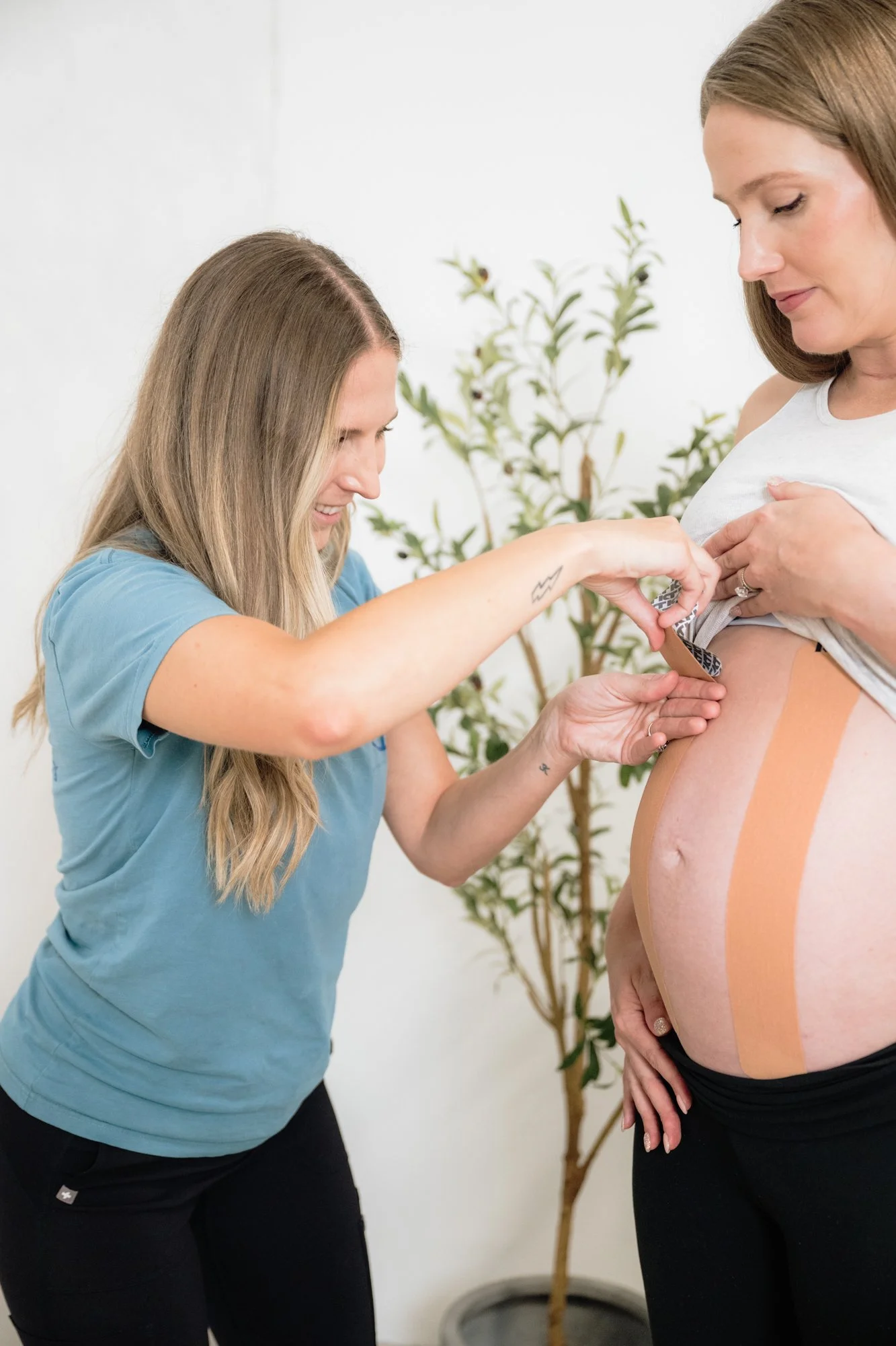 A pelvic floor therapist taping a pregnant patient's belly. 