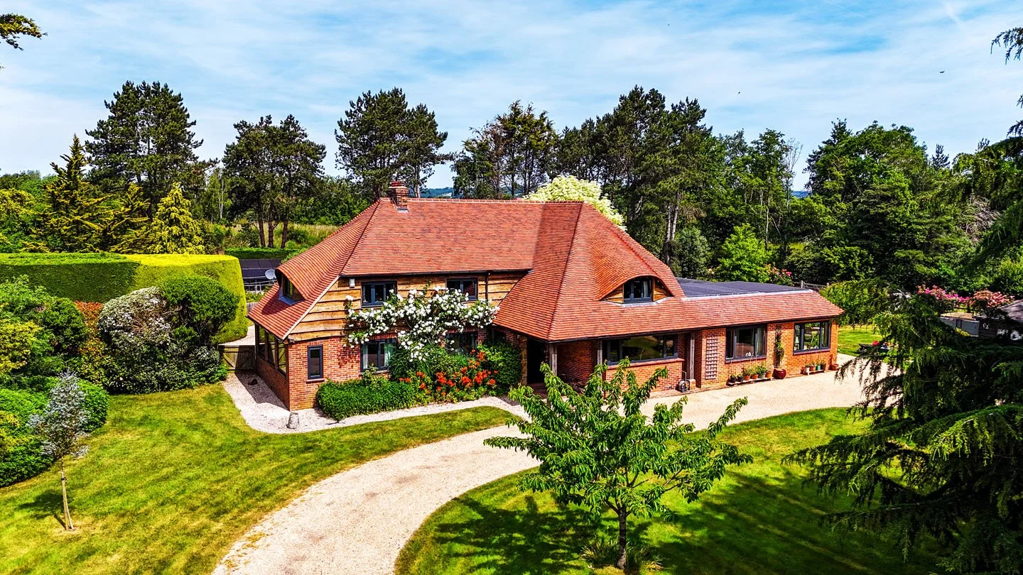 A brick house with a red-tiled roof surrounded by a well-maintained garden and trees.