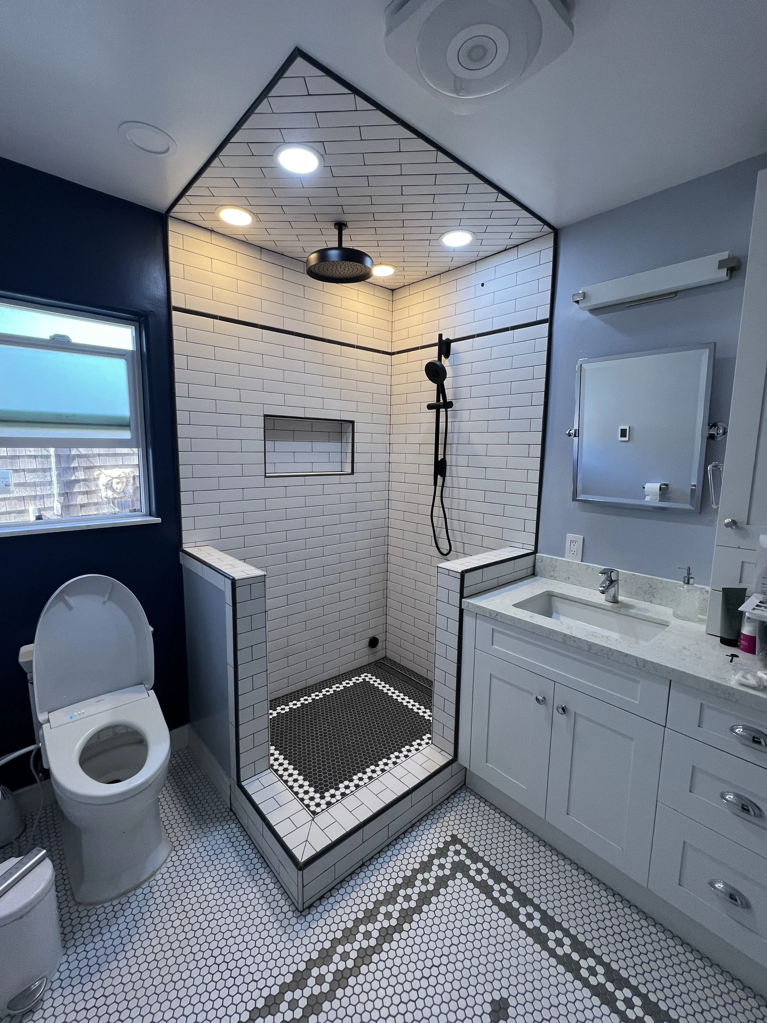 Bathroom with a shower area finished with white subway tiles, a vanity with a mirror, a toilet, and patterned tile flooring.
