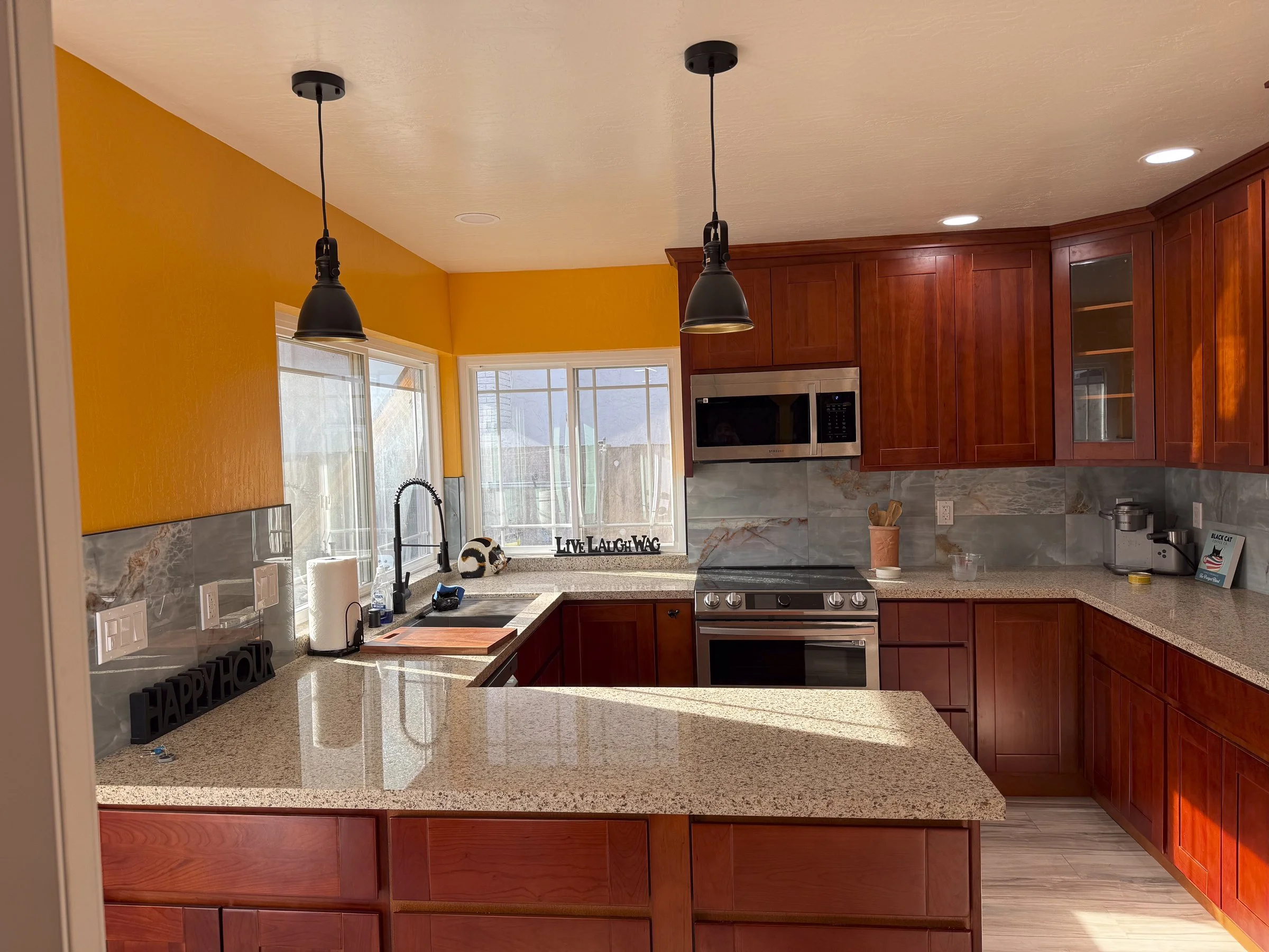 Kitchen with yellow walls, wooden cabinets, stainless steel microwave, granite countertops, and pendant lights.