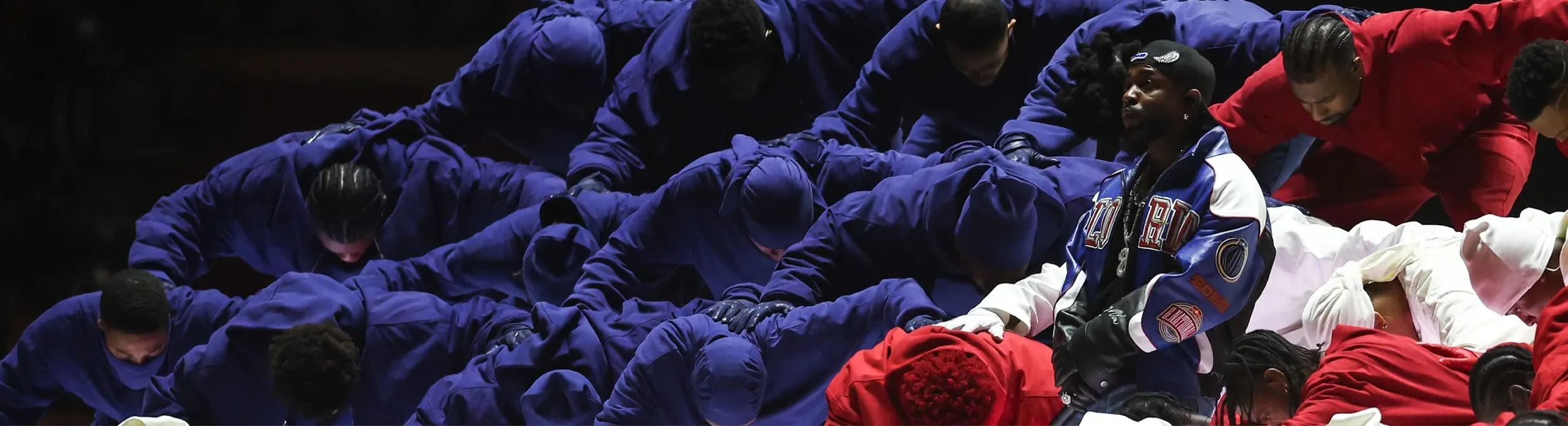 A group of young people dressed in blue, red, and white hoodies and jackets, bowing in a circle during a group activity or ceremony. They are dancers