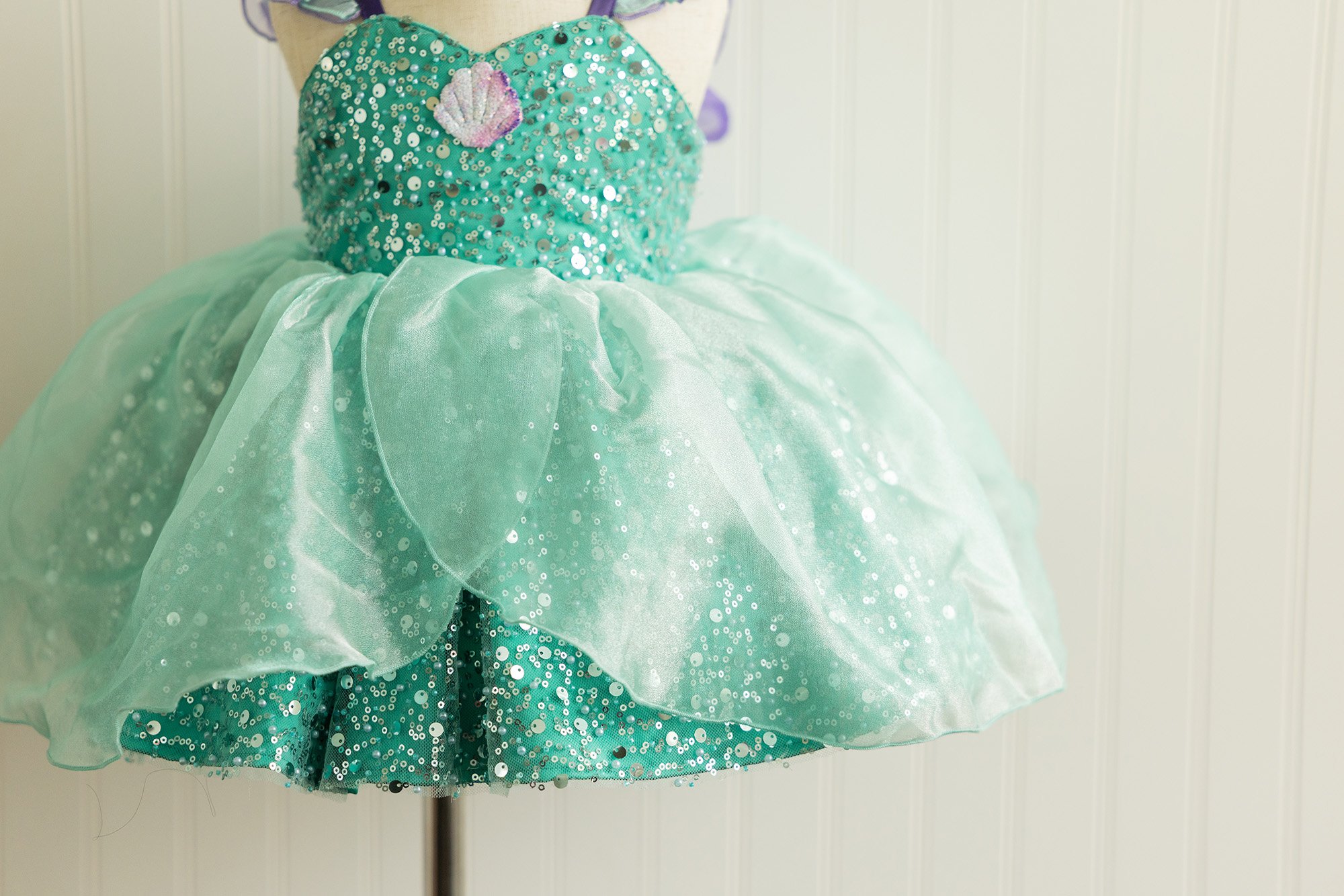 A teal sequined dress with a seashell patch on the chest, layered with a sheer, light green fabric, appears to be a children's costume or dress.