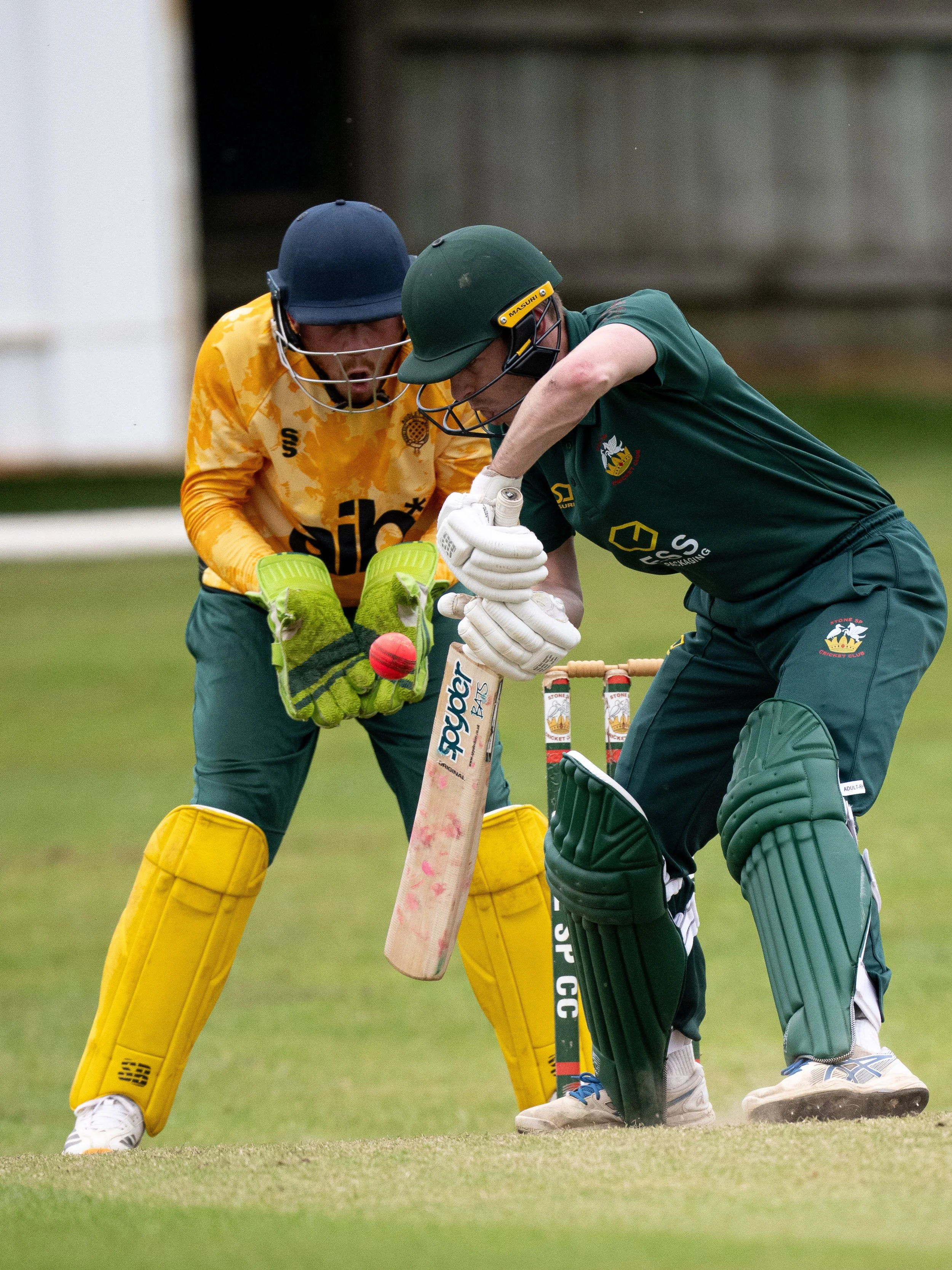 Cricket players, one in yellow protective gear and the other in green uniform, are close to each other on the cricket field during a game.