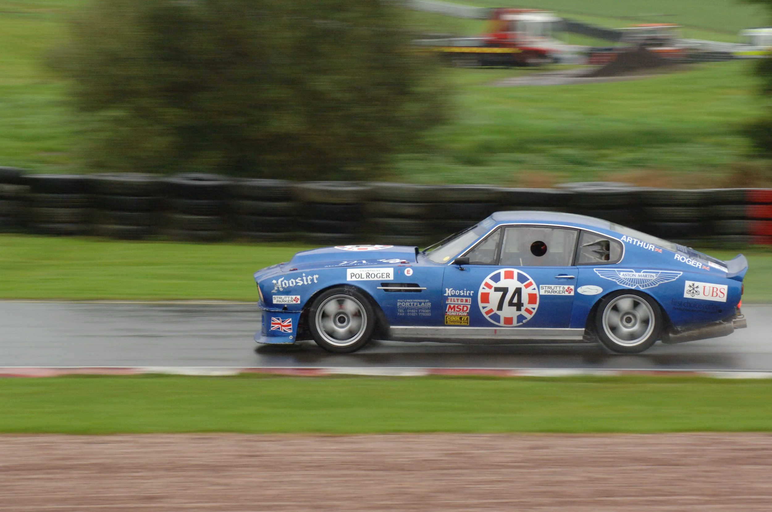A blue race car with the number 74 on its side speeding on a race track, with blurred background indicating high speed.
