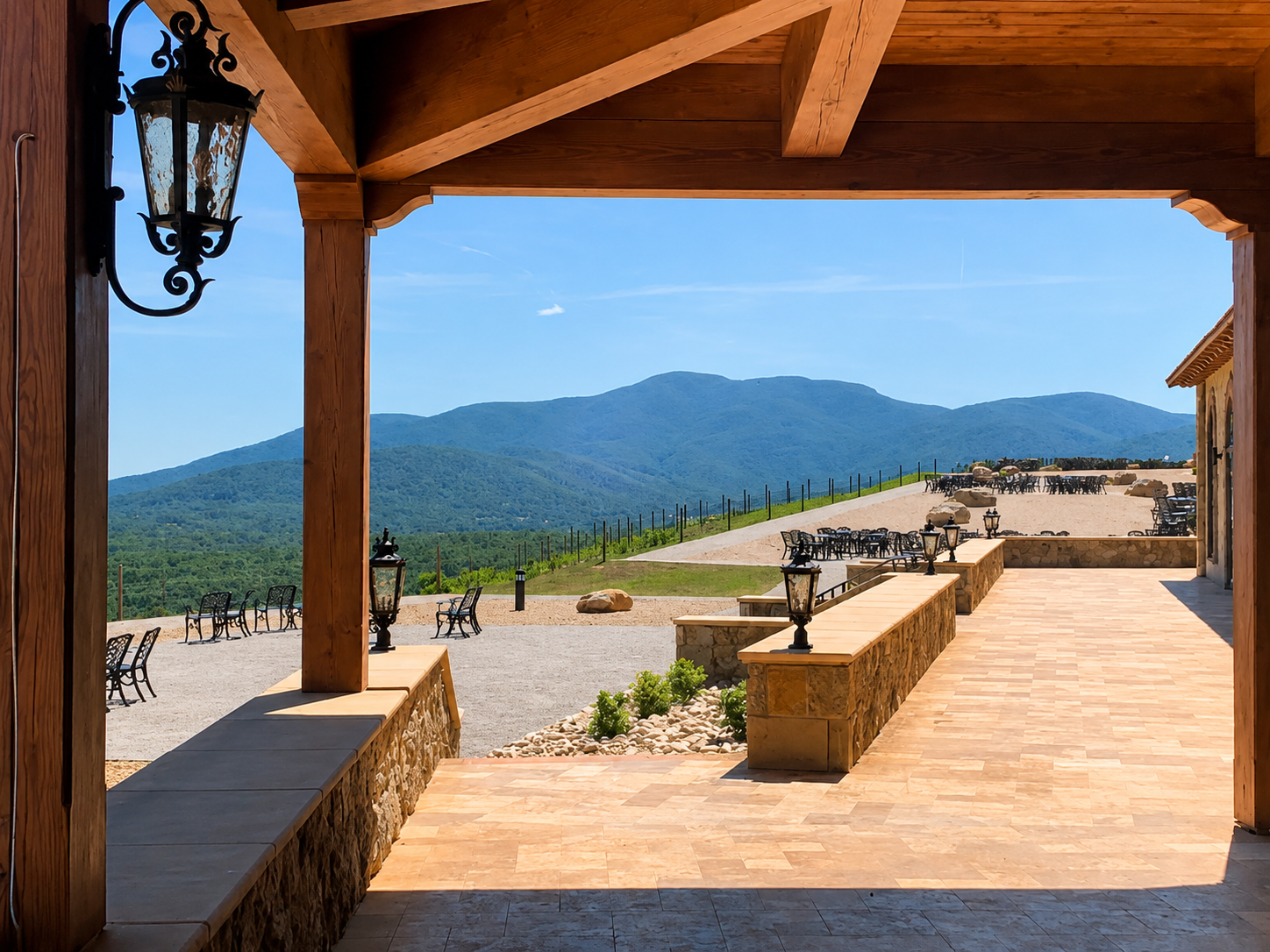 View of mountains and outdoor seating area with metal tables and chairs, from a patio framed by a wooden structure and black lanterns.
