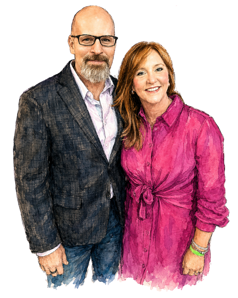 A man and woman standing together, smiling. The man has glasses, a beard, and is wearing a checked blazer and light shirt. The woman has reddish hair and is wearing a pink shirt dress with a waist tie.