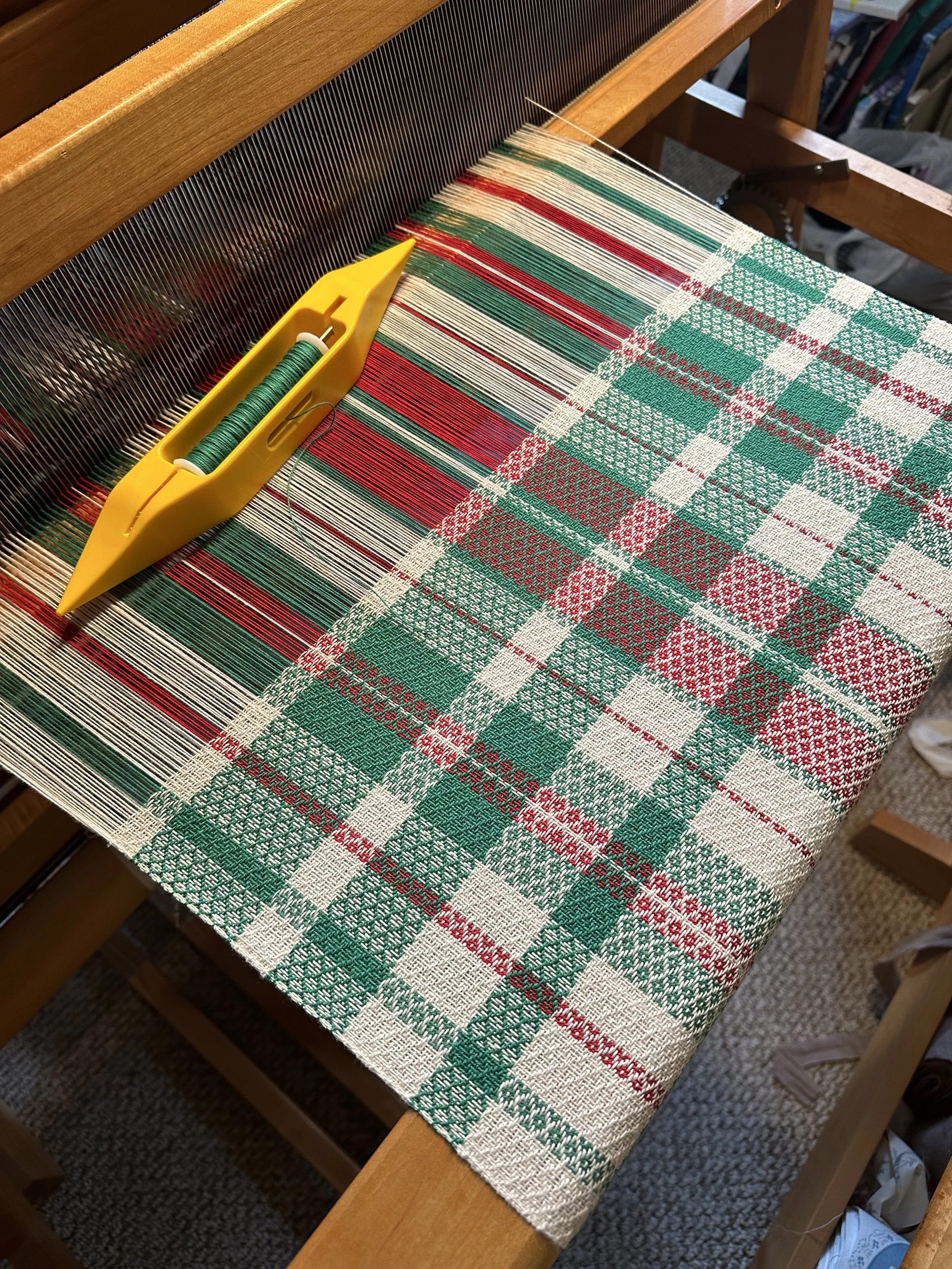 Photo of a loom with green, white, and red yarn.
