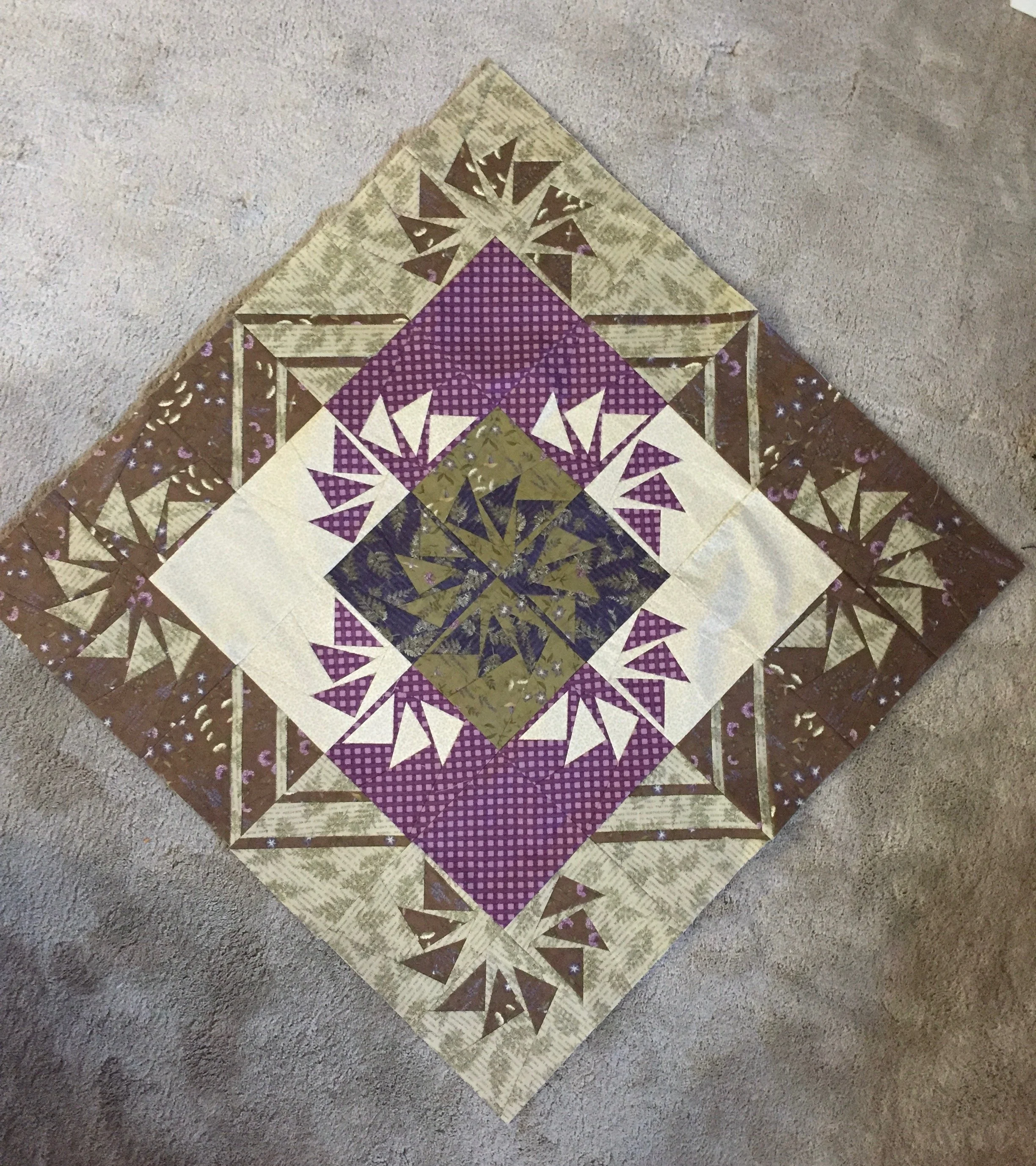A photo of a quilted square with brown, white, tan, and purple patterns.