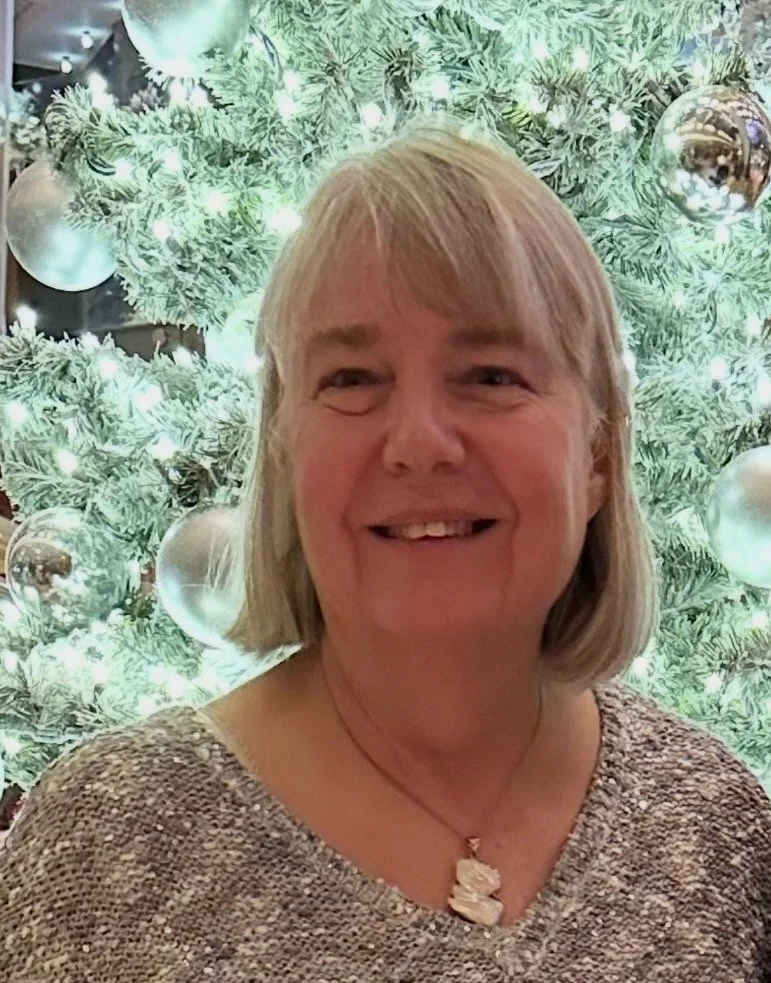 Picture of woman in front of a pastel green Christmas tree with silver ornaments.
