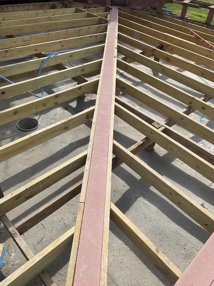 Construction site with wooden framing and pink sheathing for a building floor or deck.