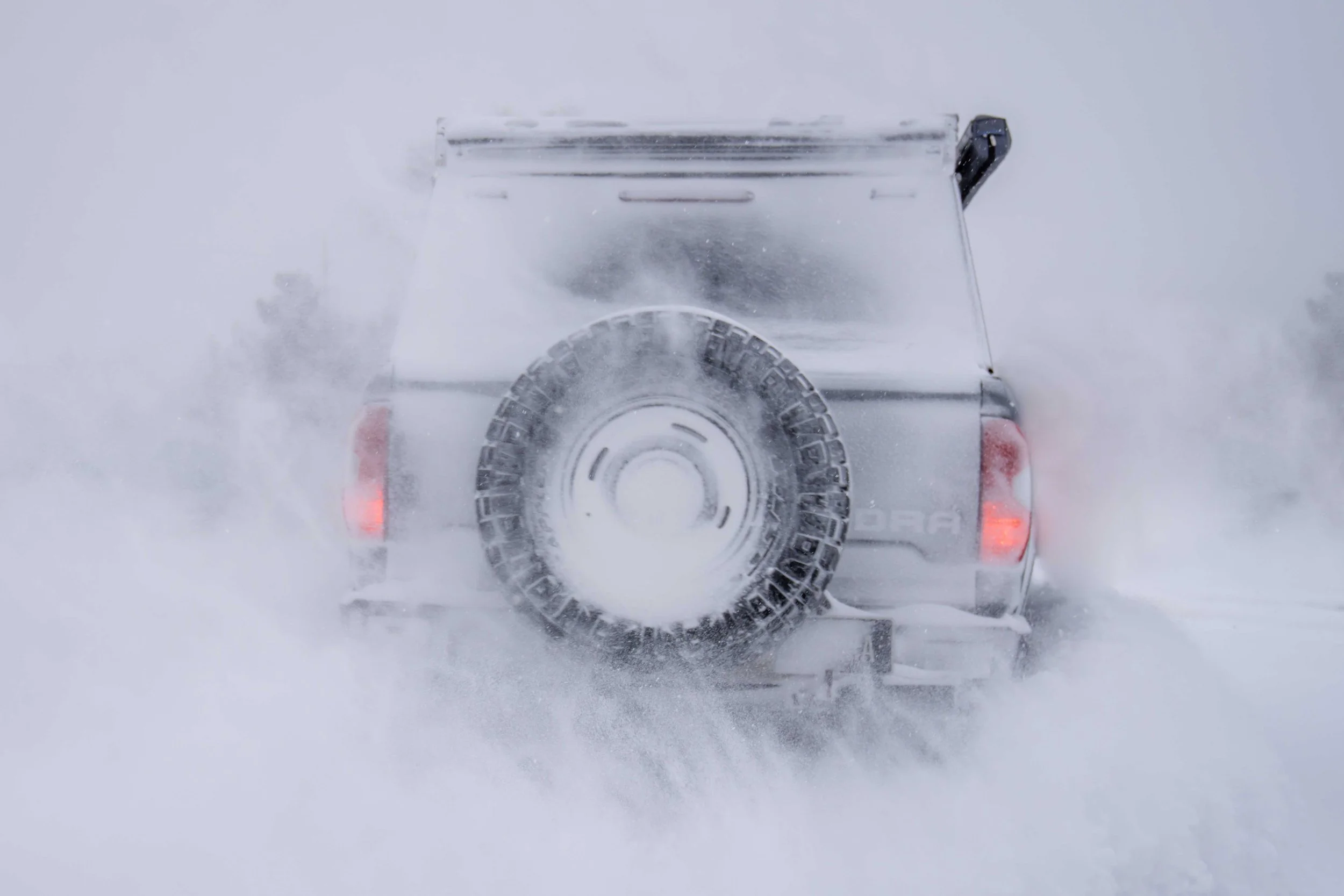 Back of a white vehicle in snow, with tire and rear lights visible.