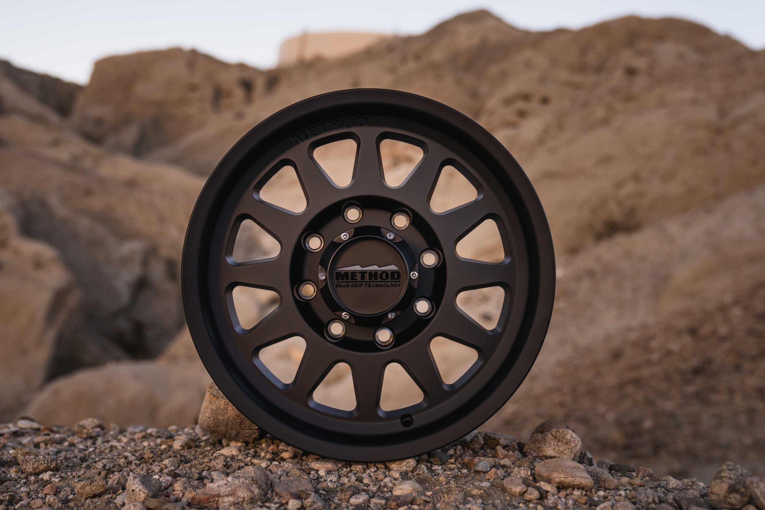 Close-up of a black Method racing wheel with a desert mountain background.