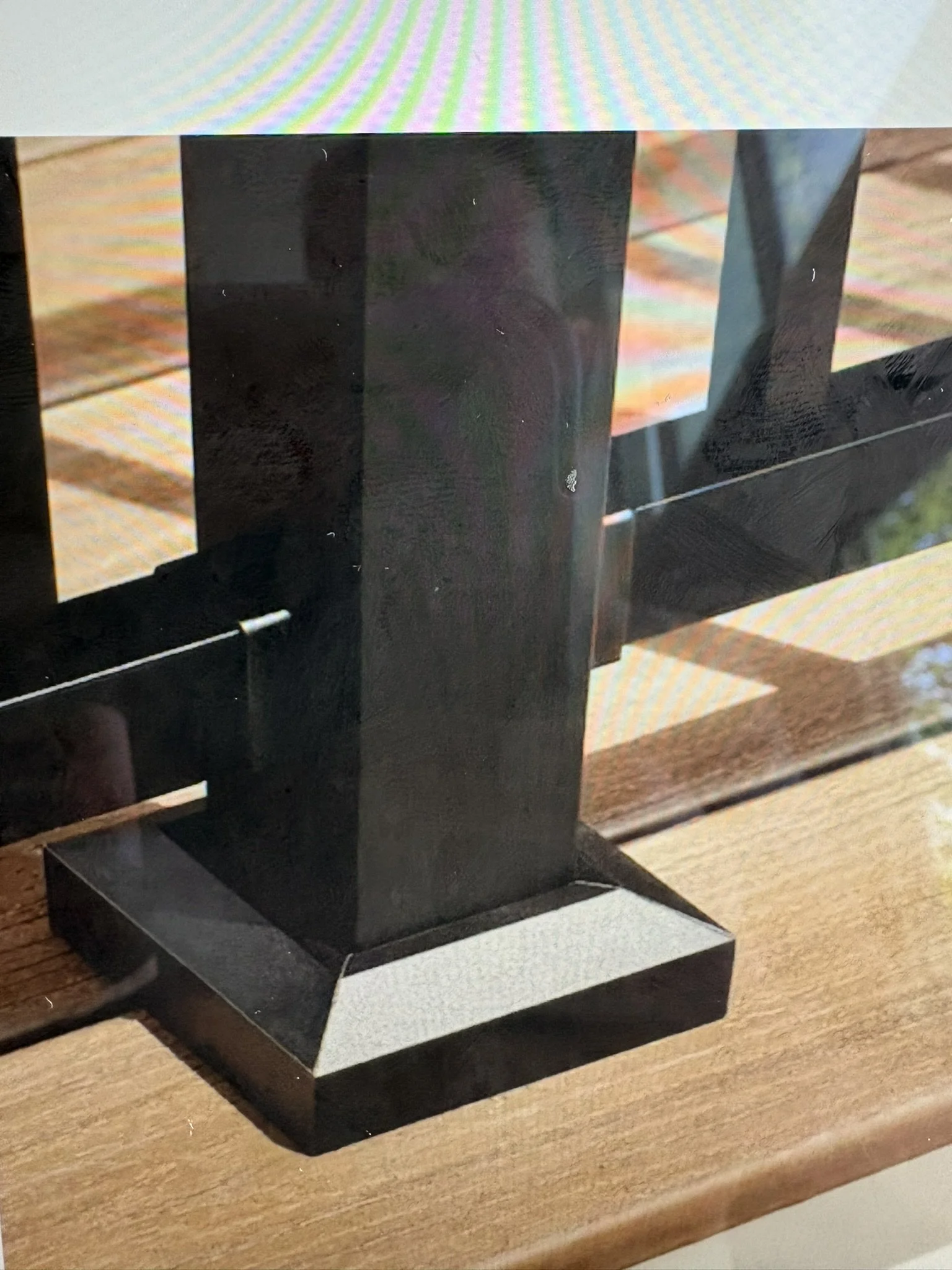 A black rectangular object with a reflective surface, placed on a wooden surface, with some industrial or workshop environment reflection visible.