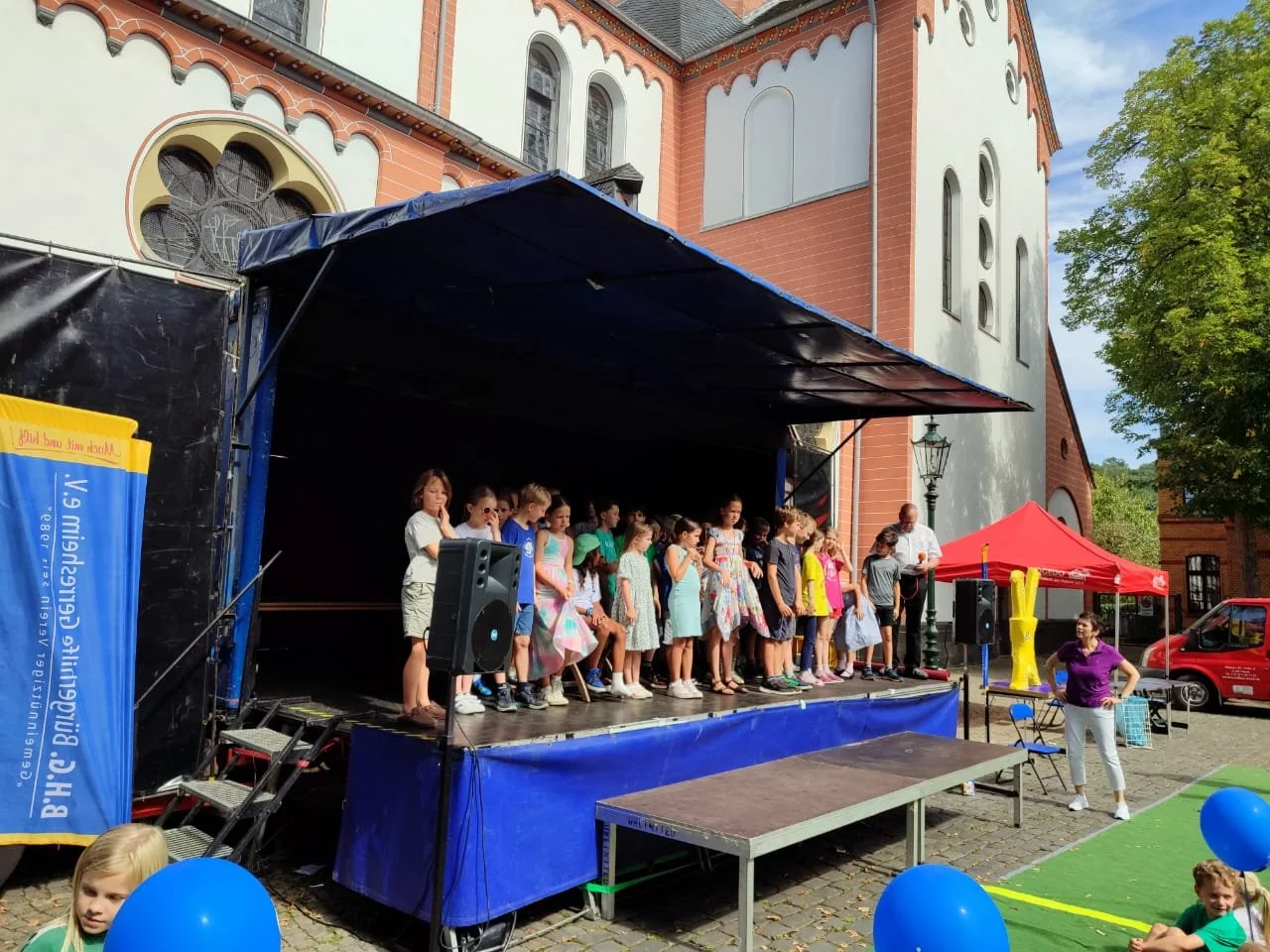 Kindergruppe bei einem Auftritt der SingPause Düsseldorf auf einer Bühne vor einer Kirche.