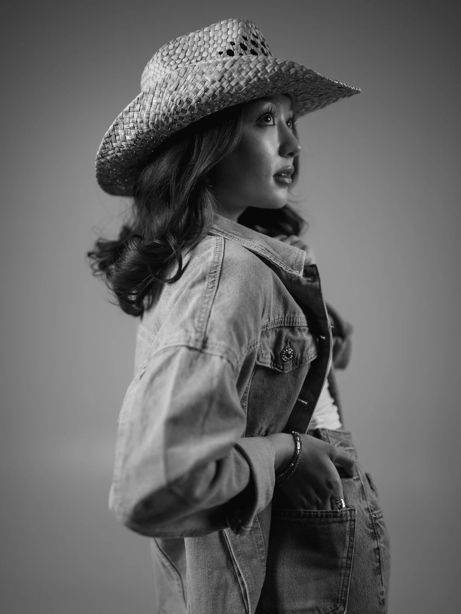 Black and white studio lighting photo of a young woman wearing a wide straw hat, a Canadian tuxedo, shot during the 2026 Nikon event held in Austin, Texas during SXSW.