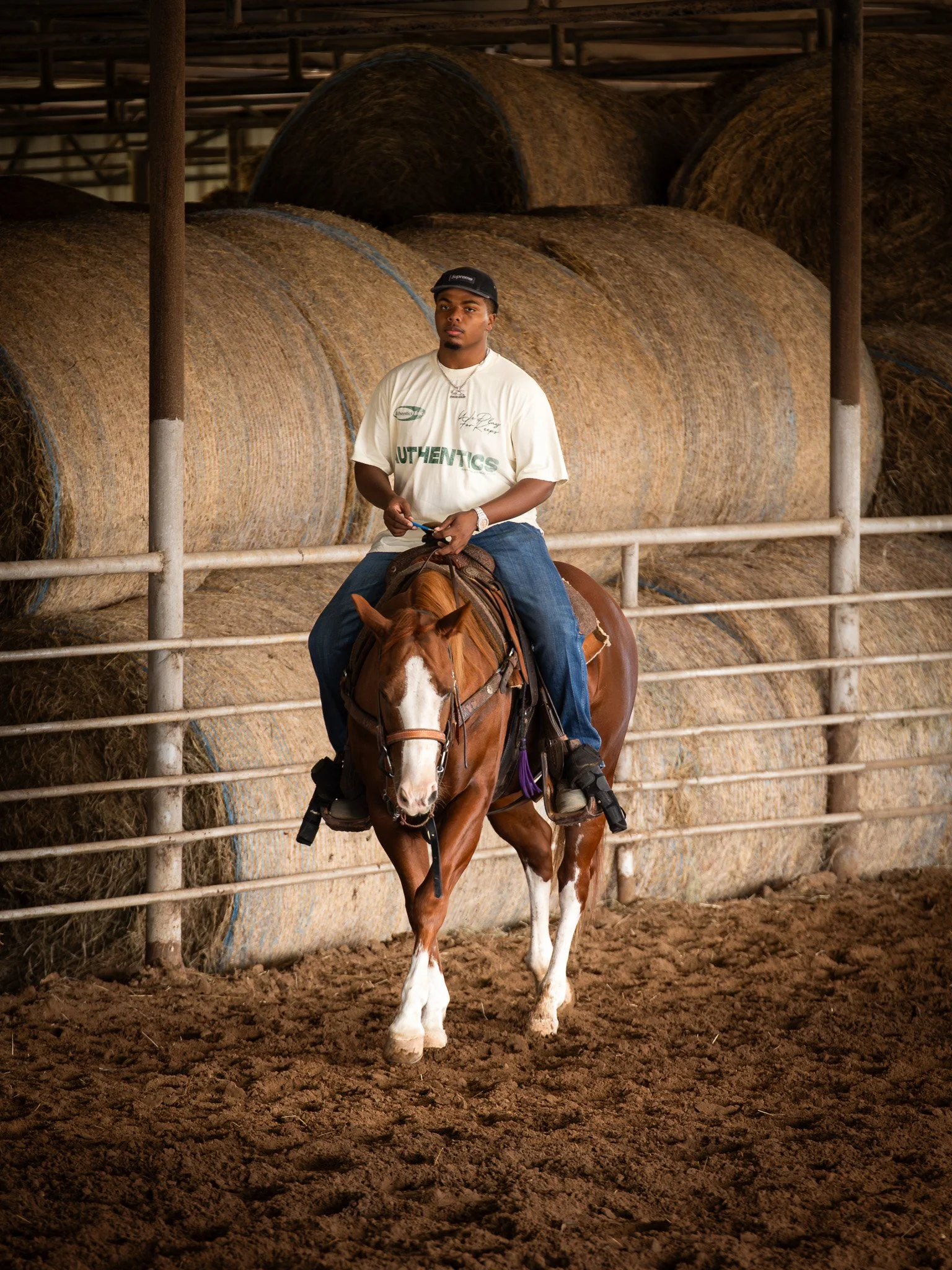 Professional roper, King Pickett riding a brown and white horse inside an indoor riding arena, with large hay bales stacked in the background.