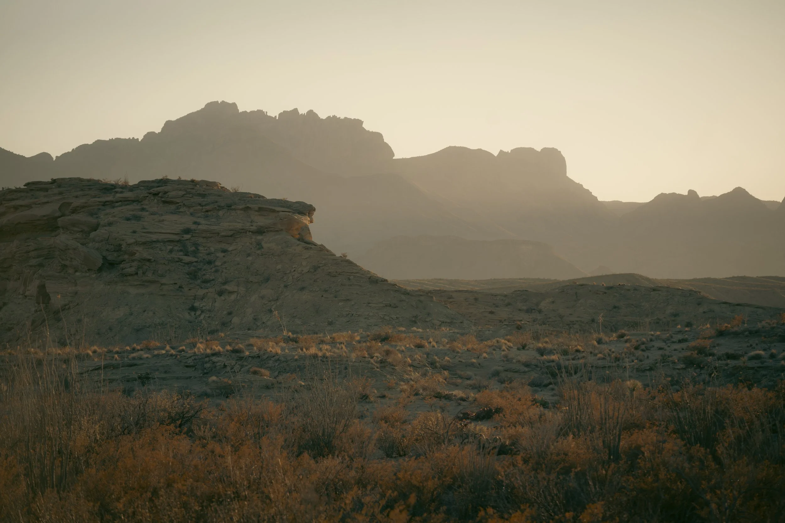 A desert landscape with rocky formations and mountains in the background during sunset or sunrise. Big Bend National Park, January 2025.