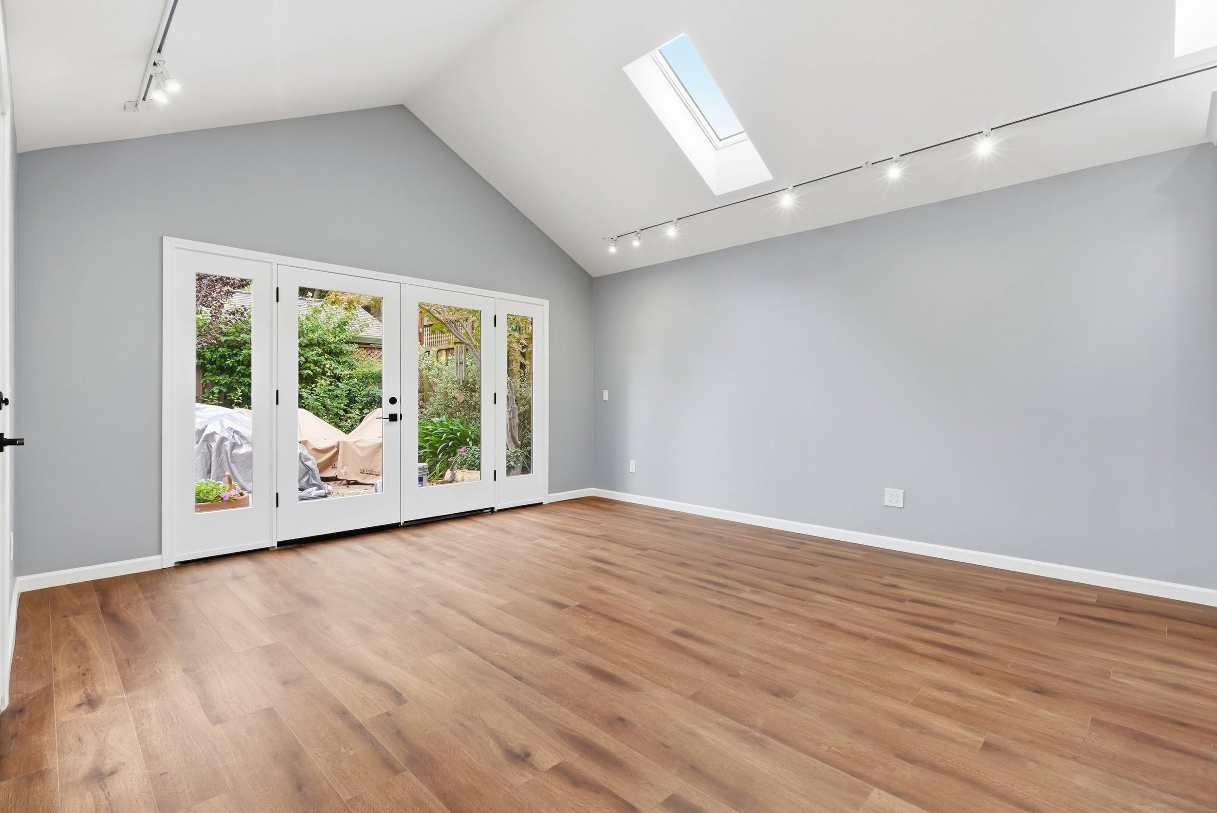Looking out from the kitchen to the living area and French doors in the Naglee Park ADU. The floors are hardwood and the walls gray. On the ceiling there are skylights and track lighting.