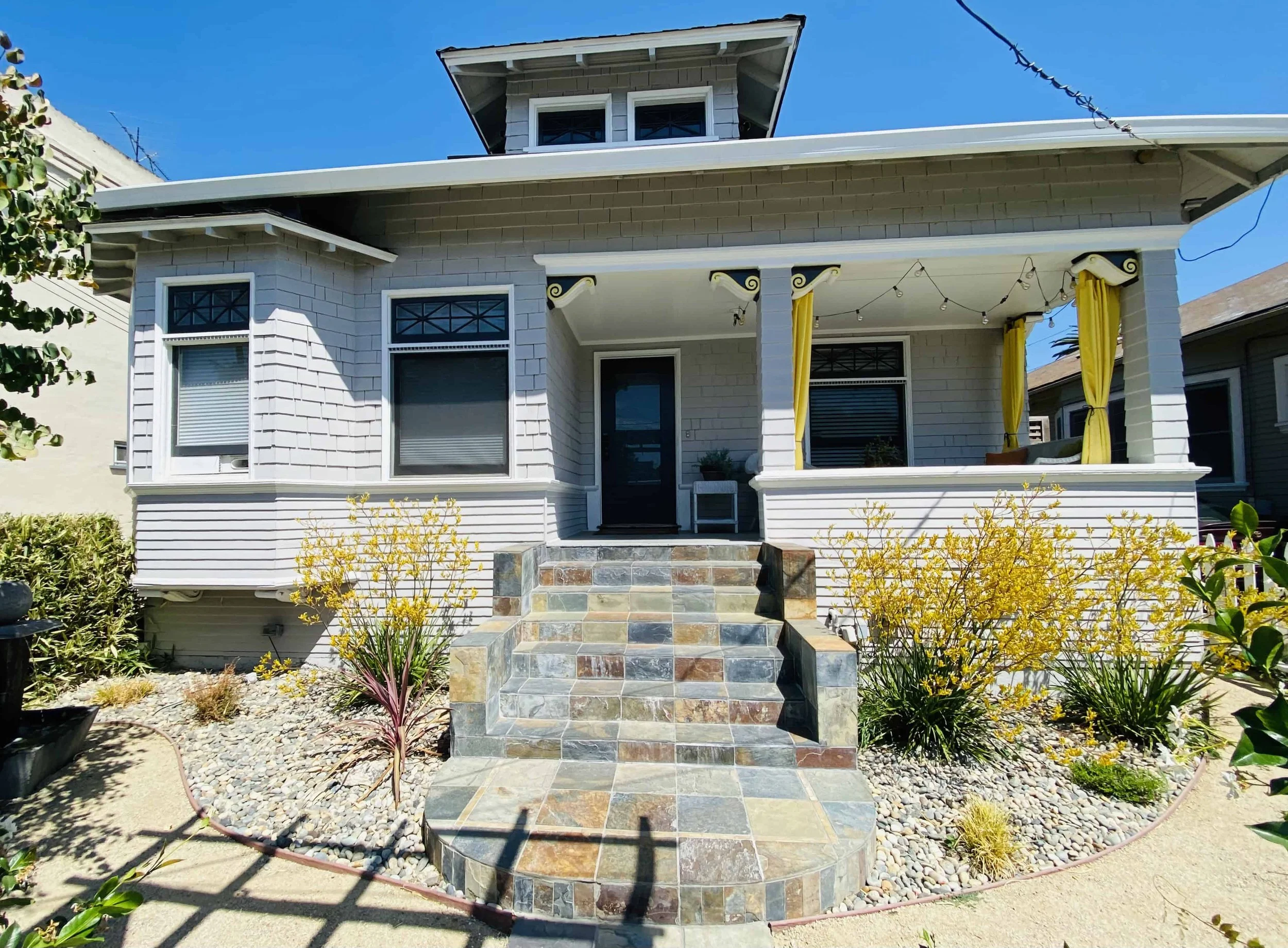 Historic San Jose home with a stone walkway and steps, painted in gray with the large porch painted white.