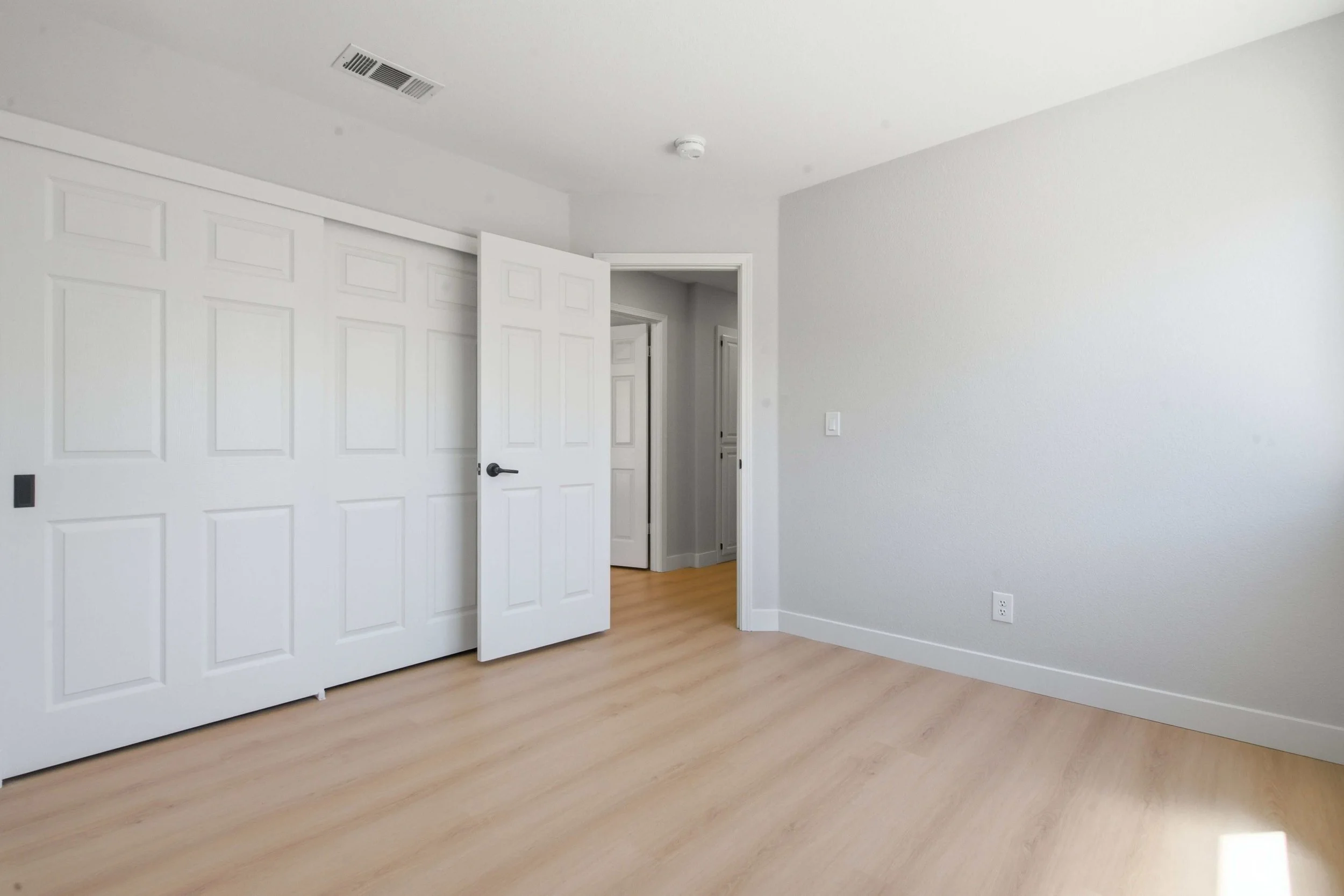 Freshly renovated condominium bedrooms looking from the inside toward the door. On the left are new white closet doors and the right a gray wall.