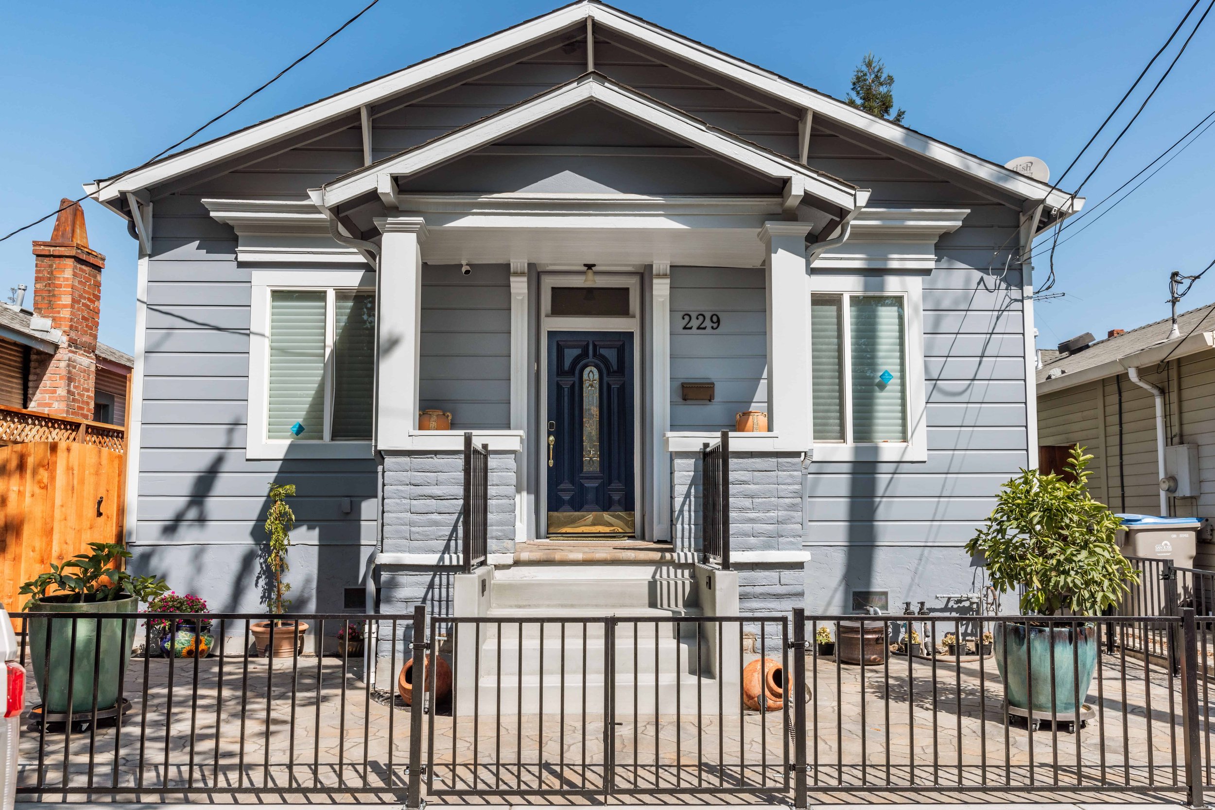 Historic San Jose home newly painted in gray and siding repair. The front yard has a decorative metal fence and potted plants.