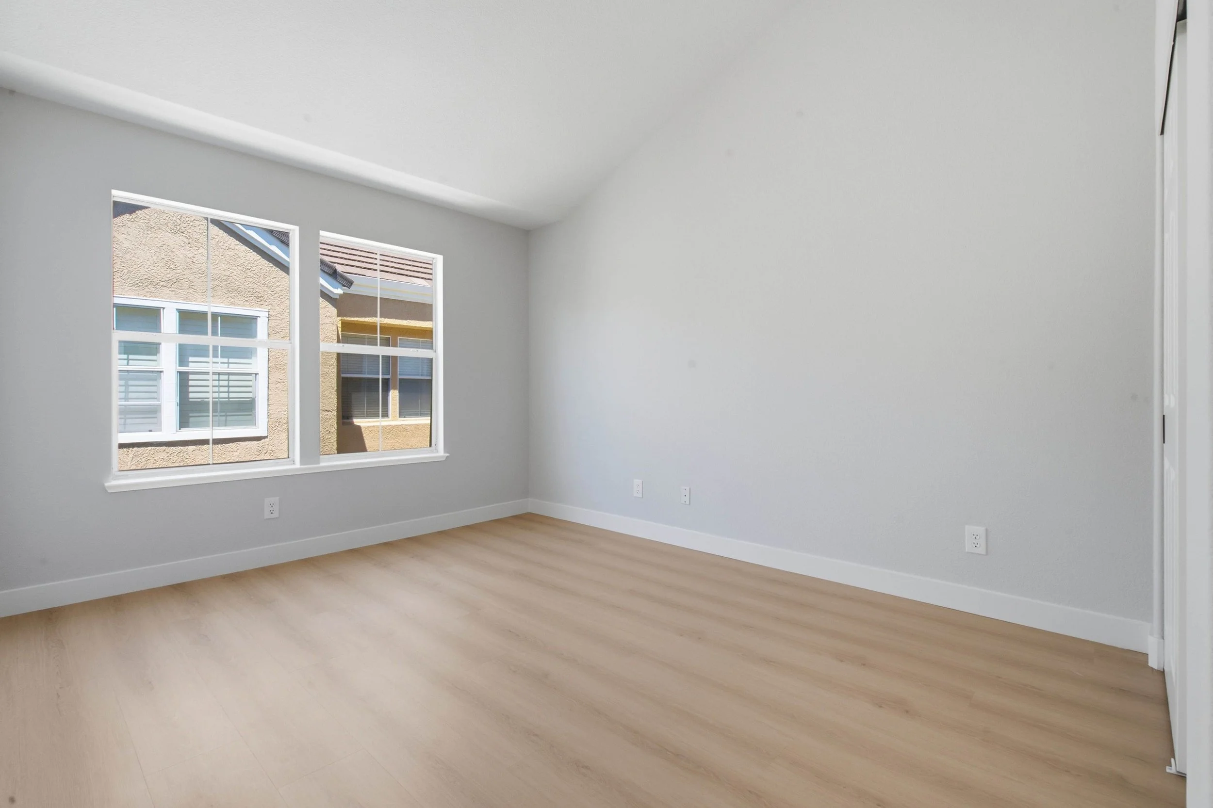 Interior of a bedroom in a Bay Area condo renovation. This overlooks the street with a large window and wood floors.