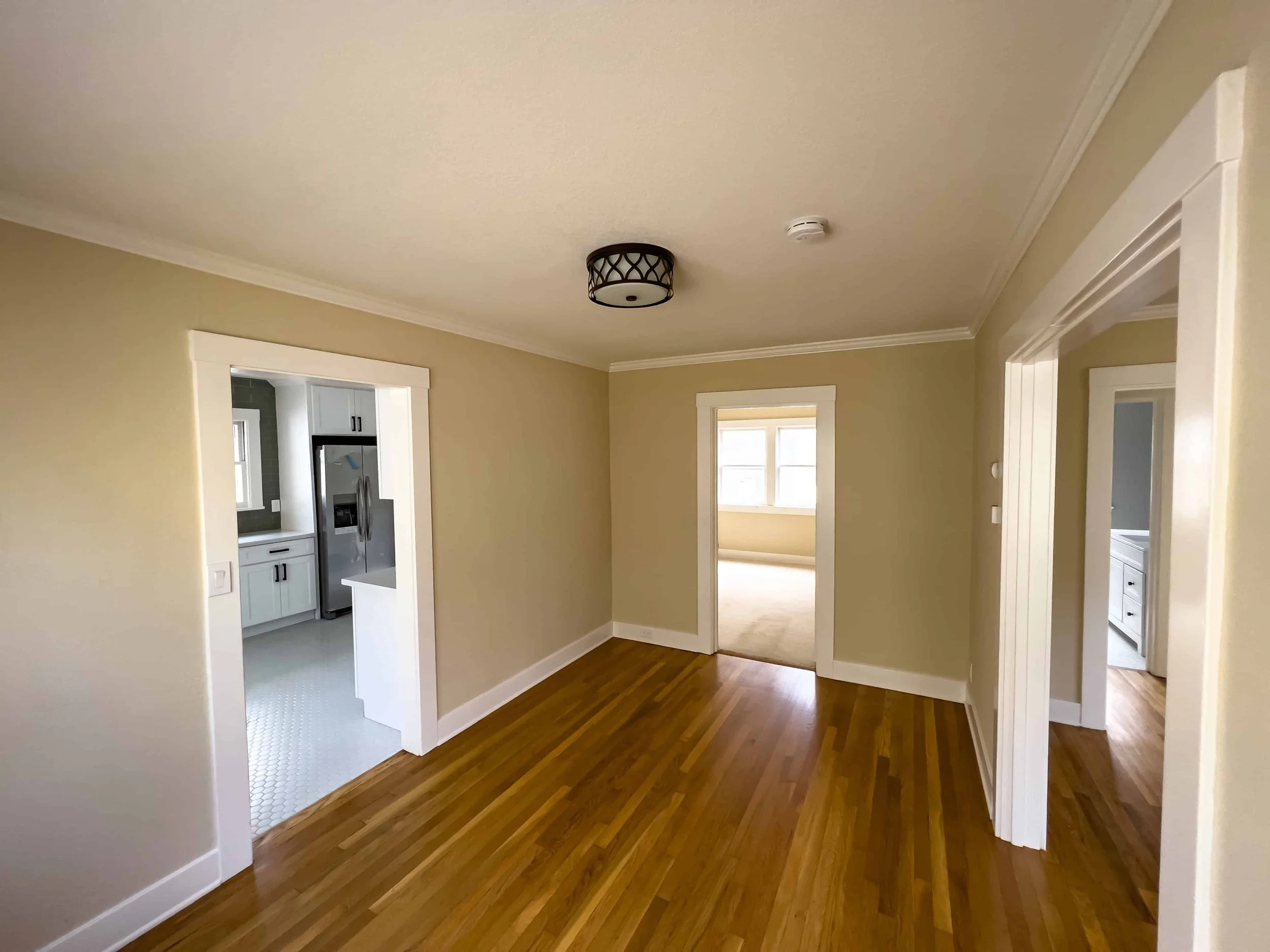 Craftsman dining area with refinished wood floors and newly painted beige walls. The room is empty and the kitchen is visible through the doorway.