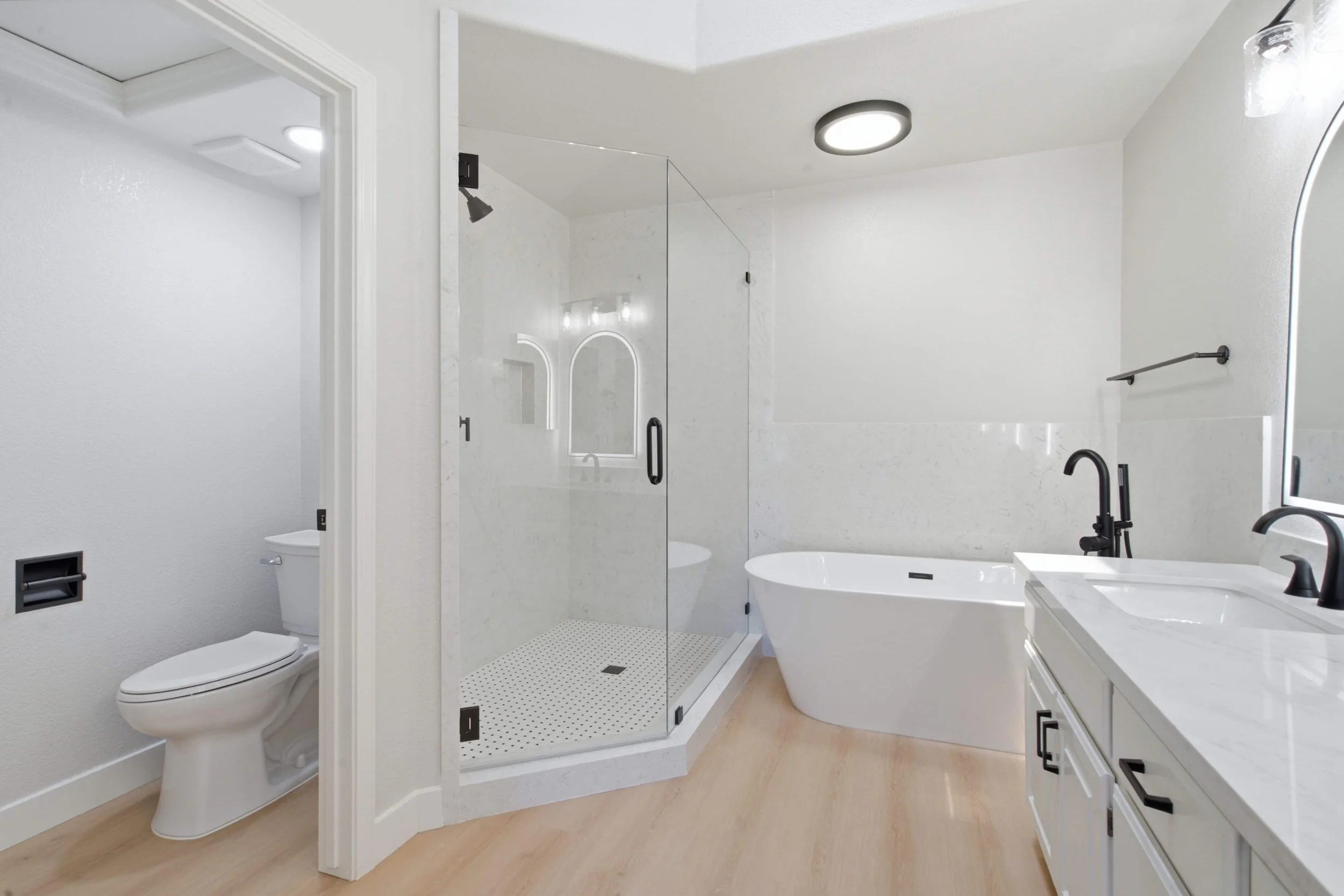 Renovated master bathroom in a Silicon Valley condominium. This view show the toilet, walk-in shower, soaking tub and new cabinets. The room has oiled brass finishing and a wood floor.