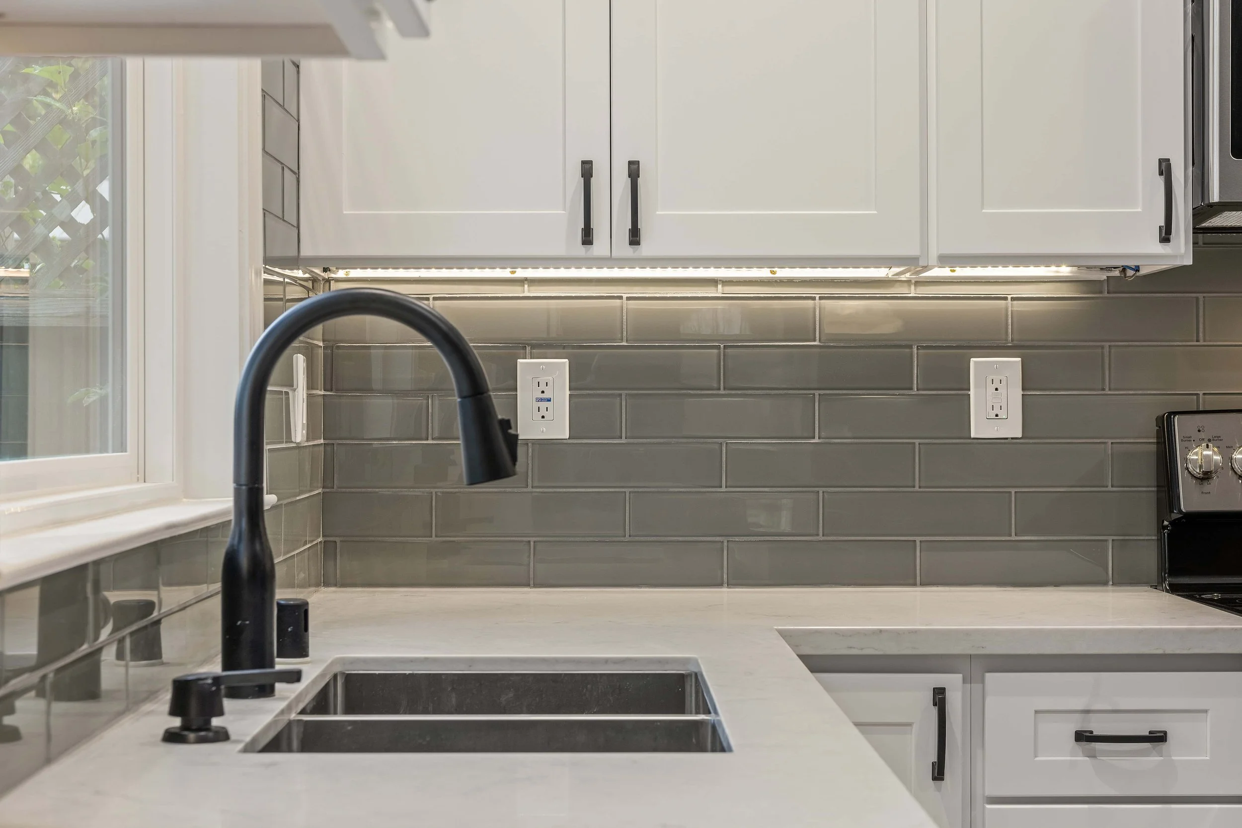 Gray subway tiles with marble countertops and a matte black kitchen faucet.