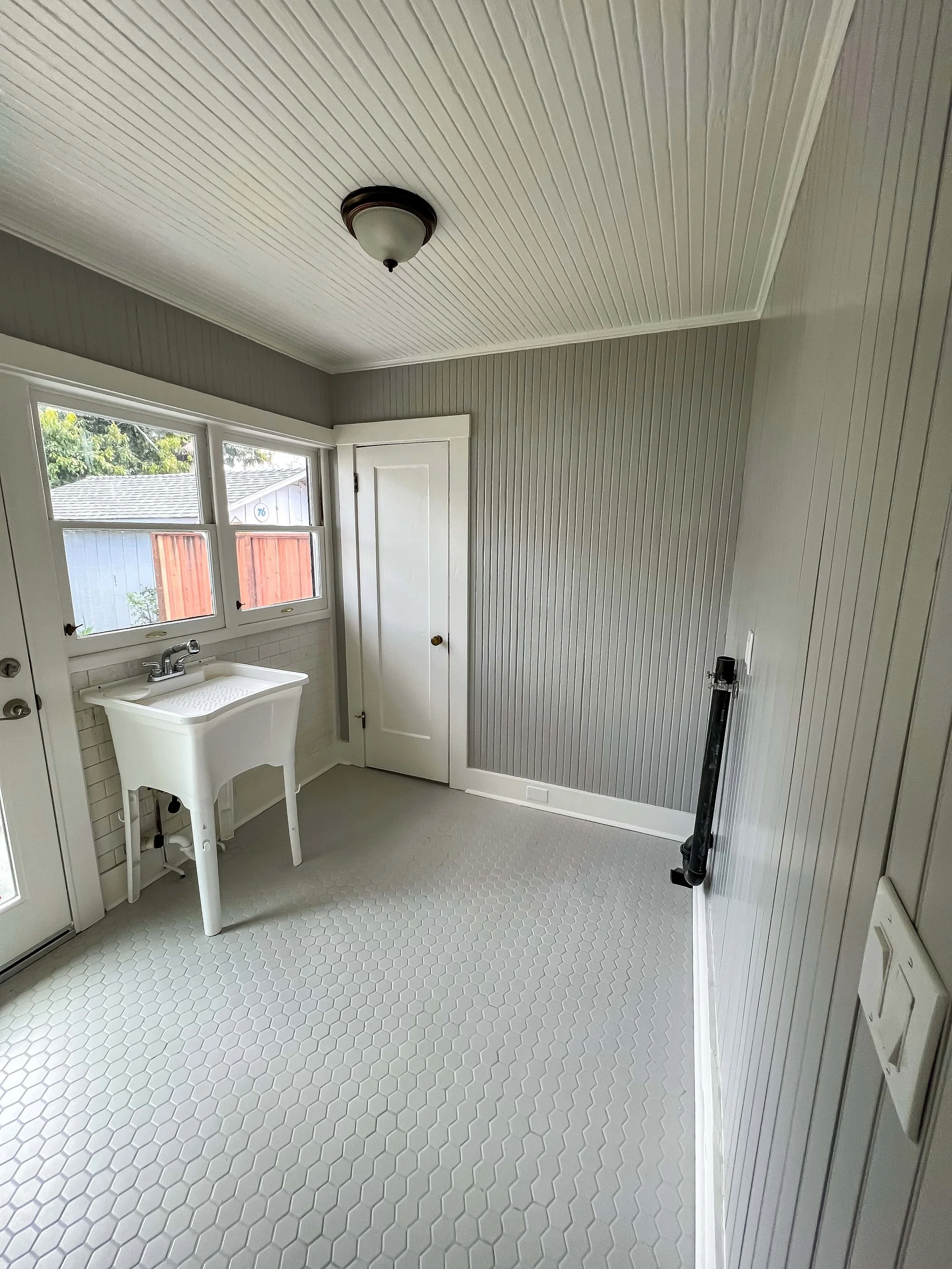 Interior of a craftsman cottage enclosed porch that has a sink and tile floors. The walls are painted gray.