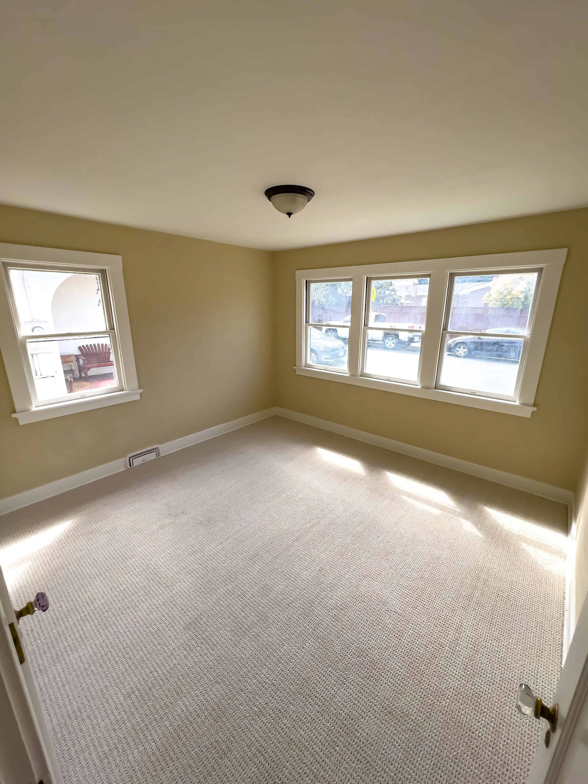 Restored craftsman cottage bedroom, empty with new carpet and windows overlooking the street.