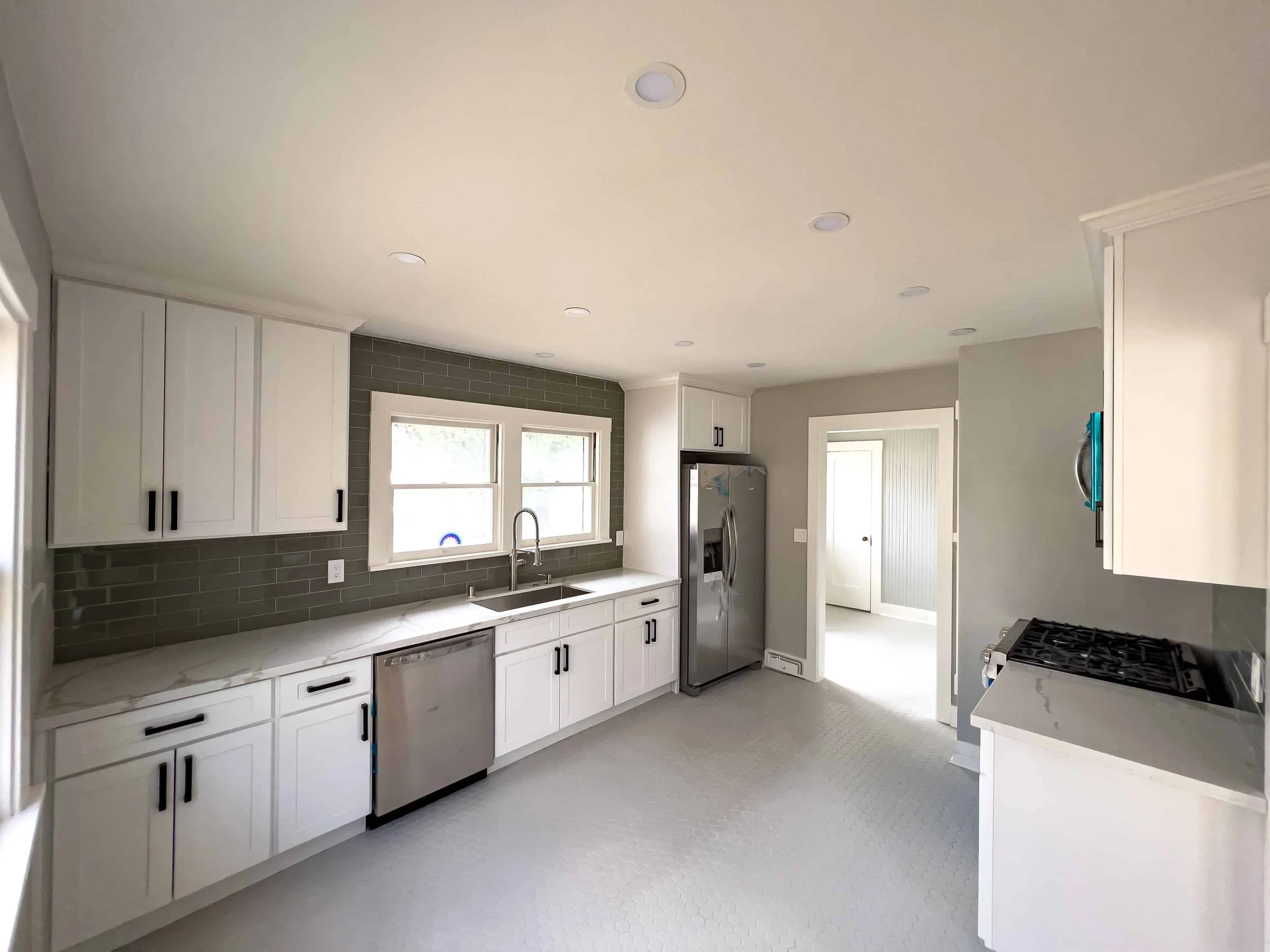 Craftsman cottage new kitchen remodel with white cabinets, stainless appliances, and gray tiles.