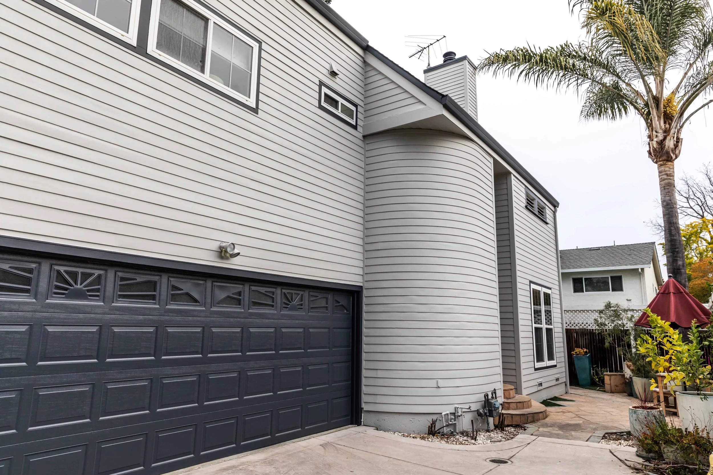 Side of a grey house in San Jose with dark grey garage door and palm tree in the background.