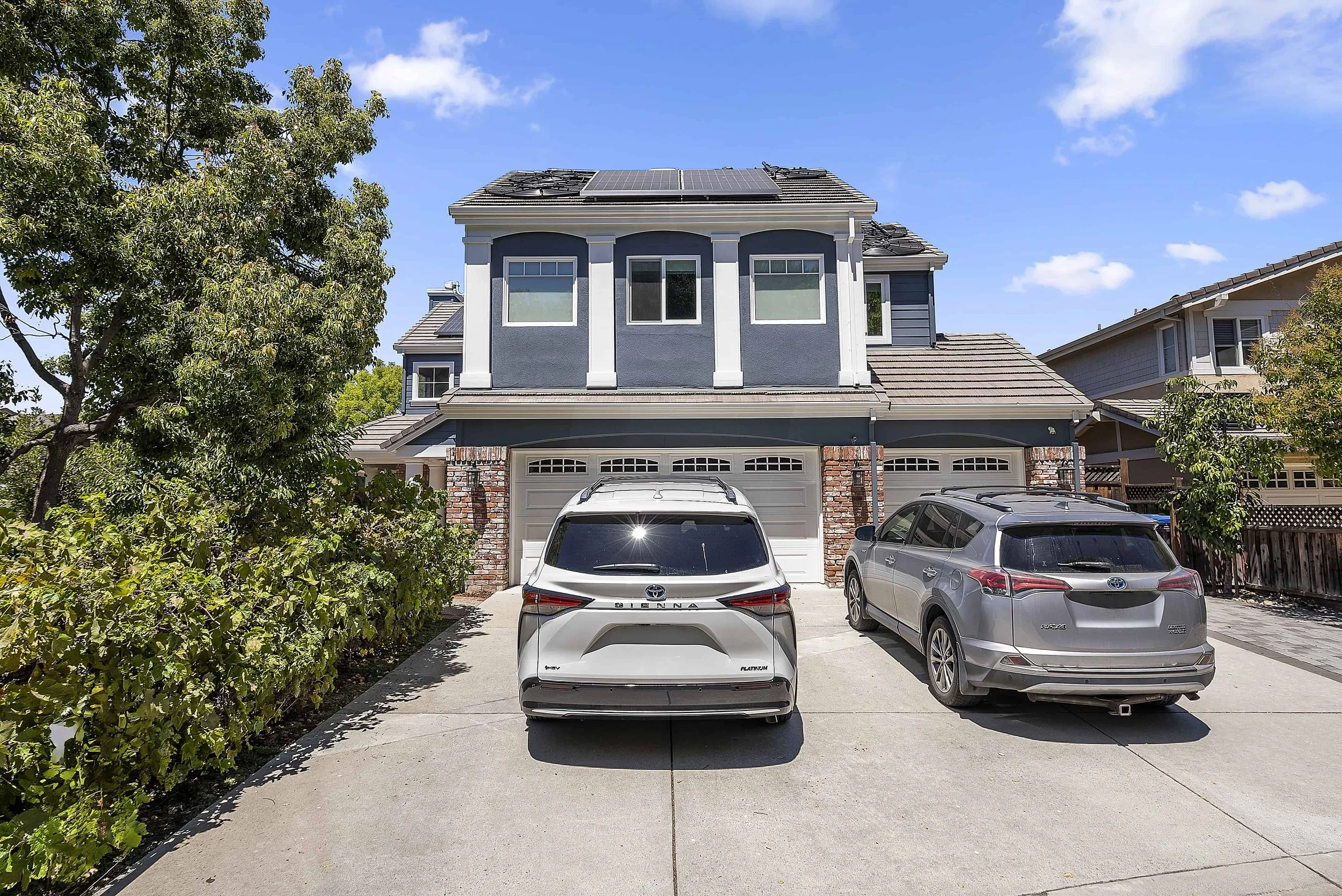 Two story house with new siding in gray with while pillars and white garage doors with cars in driveway.