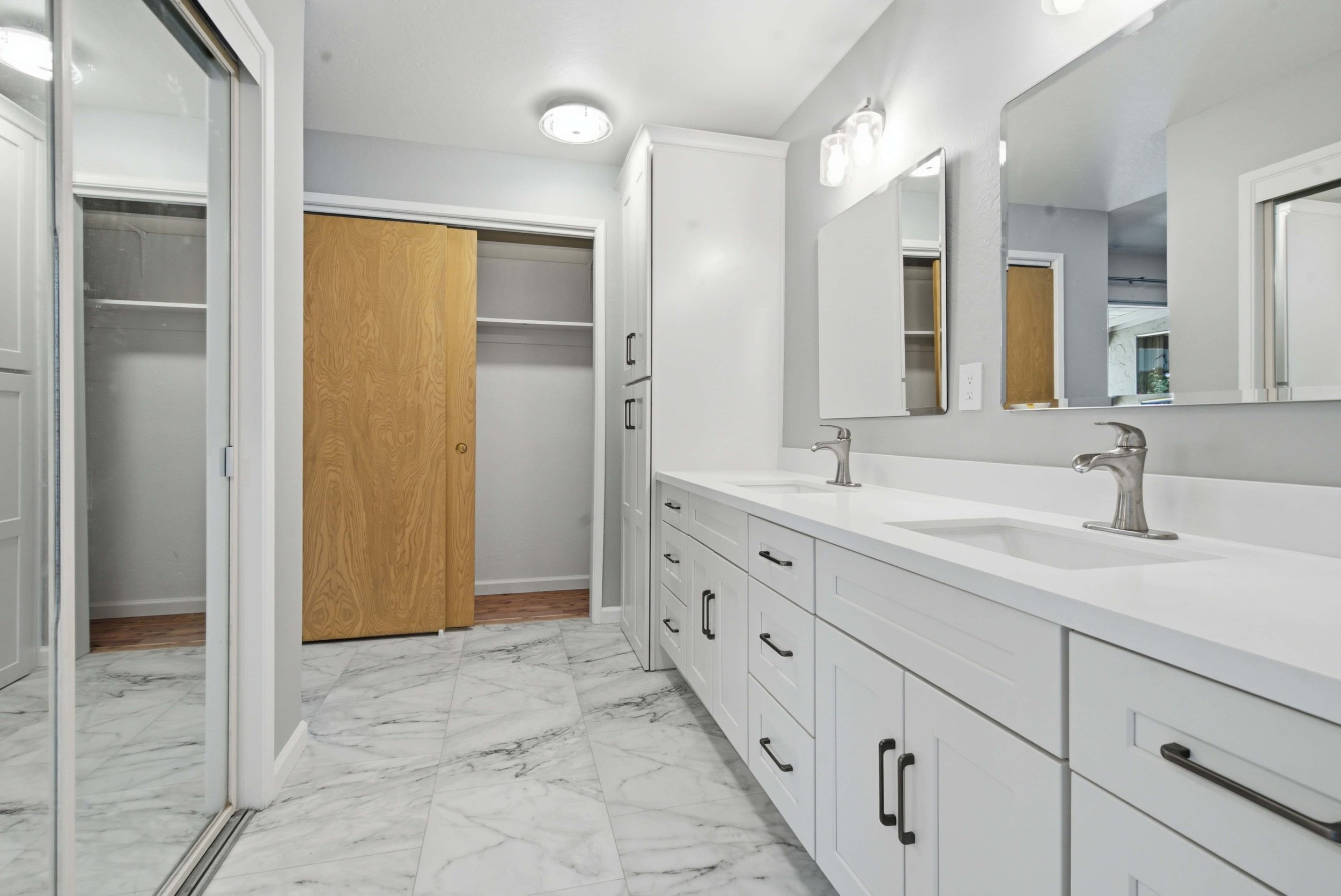 Renovated bathroom with bright lighting. The vanity features double sinks and the closet is mirrored.