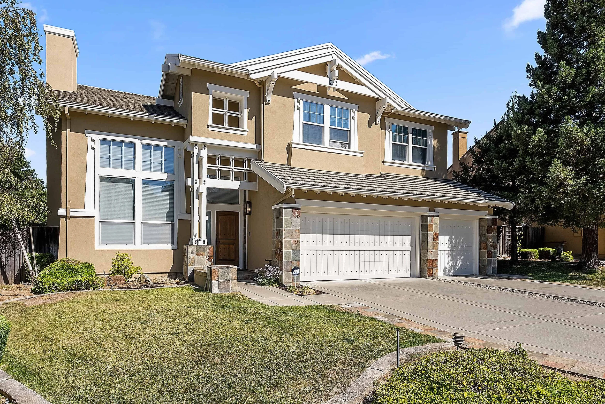 Large tan house with two white garage doors and stone facing on the pillars.