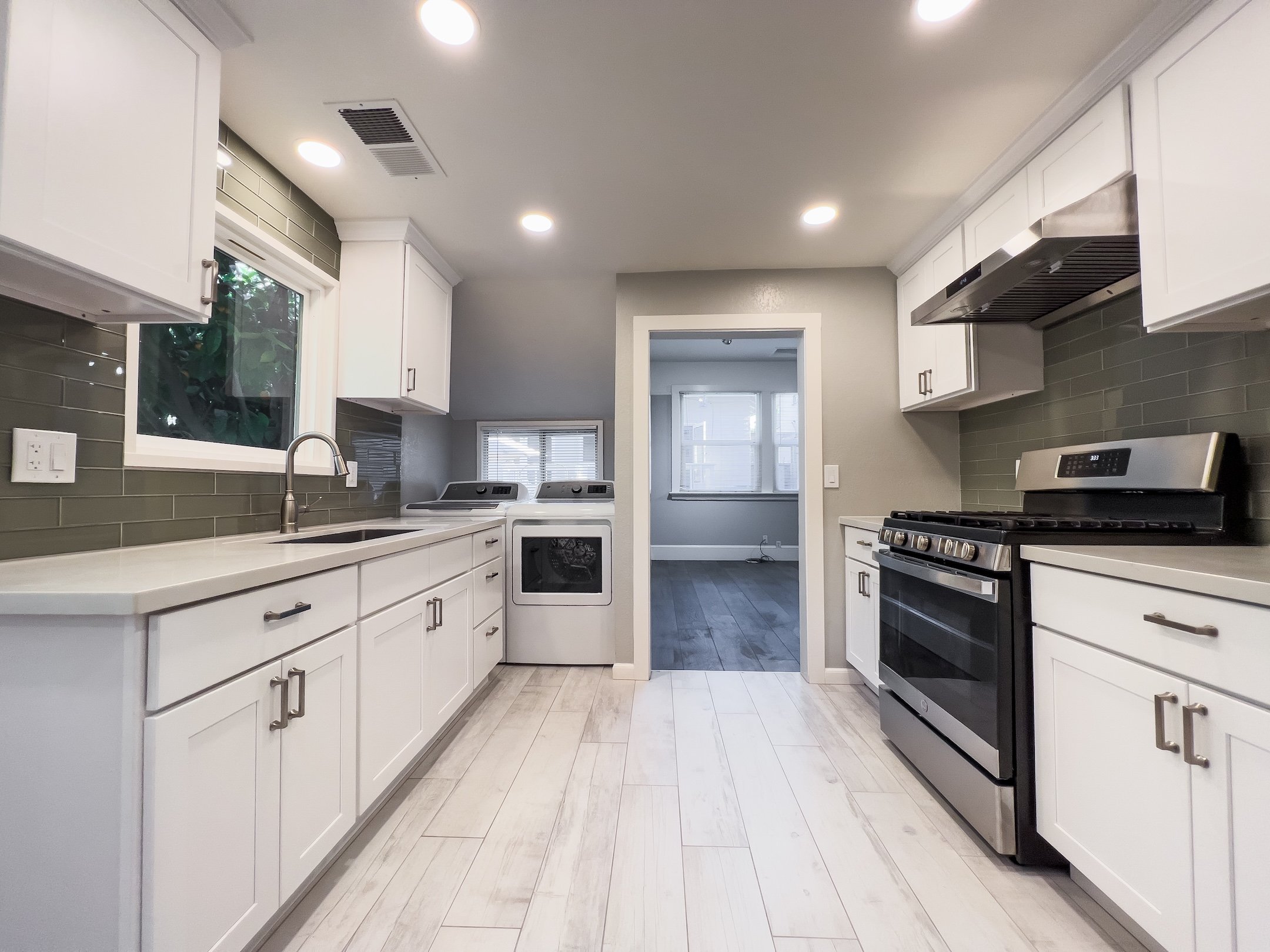 Kitchen with white cabinets, gray backsplash, stainless steel appliances, and a window overlooking greenery.