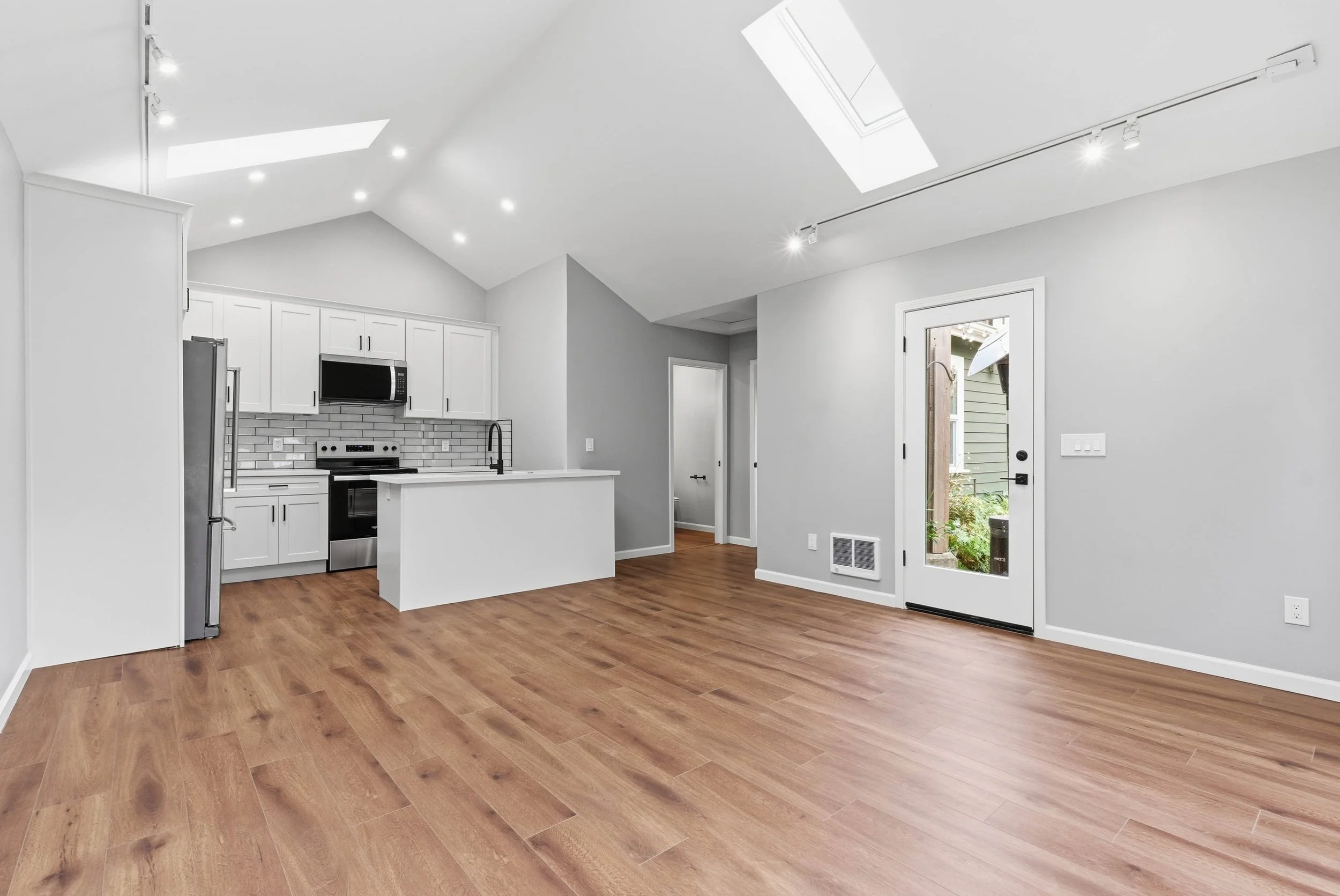 ADU interior with hardwood floors and glass exterior door. The kitchen and white kitchen island are in the background.