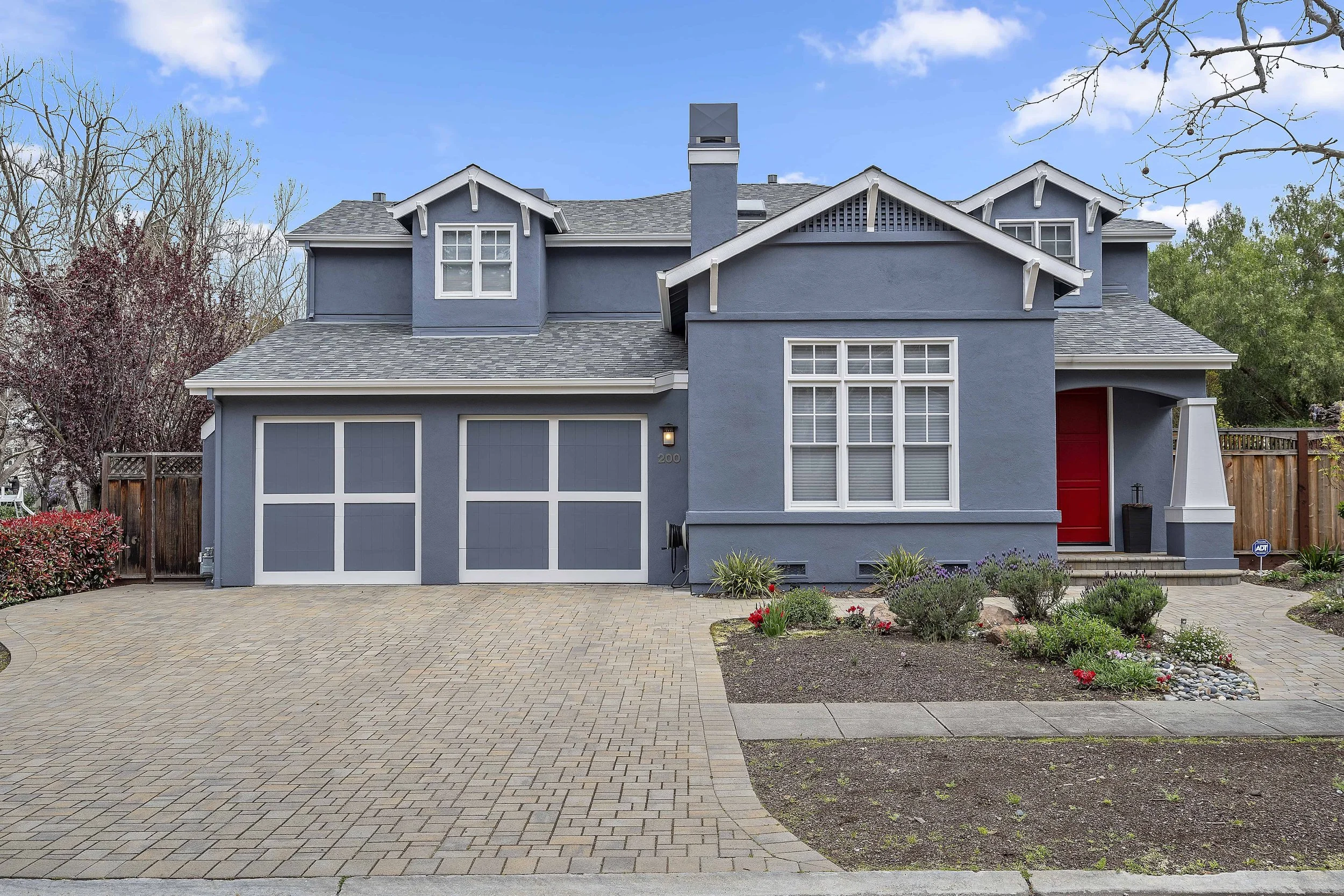 Freshly painted slate blue two story house with white trim and a red front door. There is a large brick driveway.