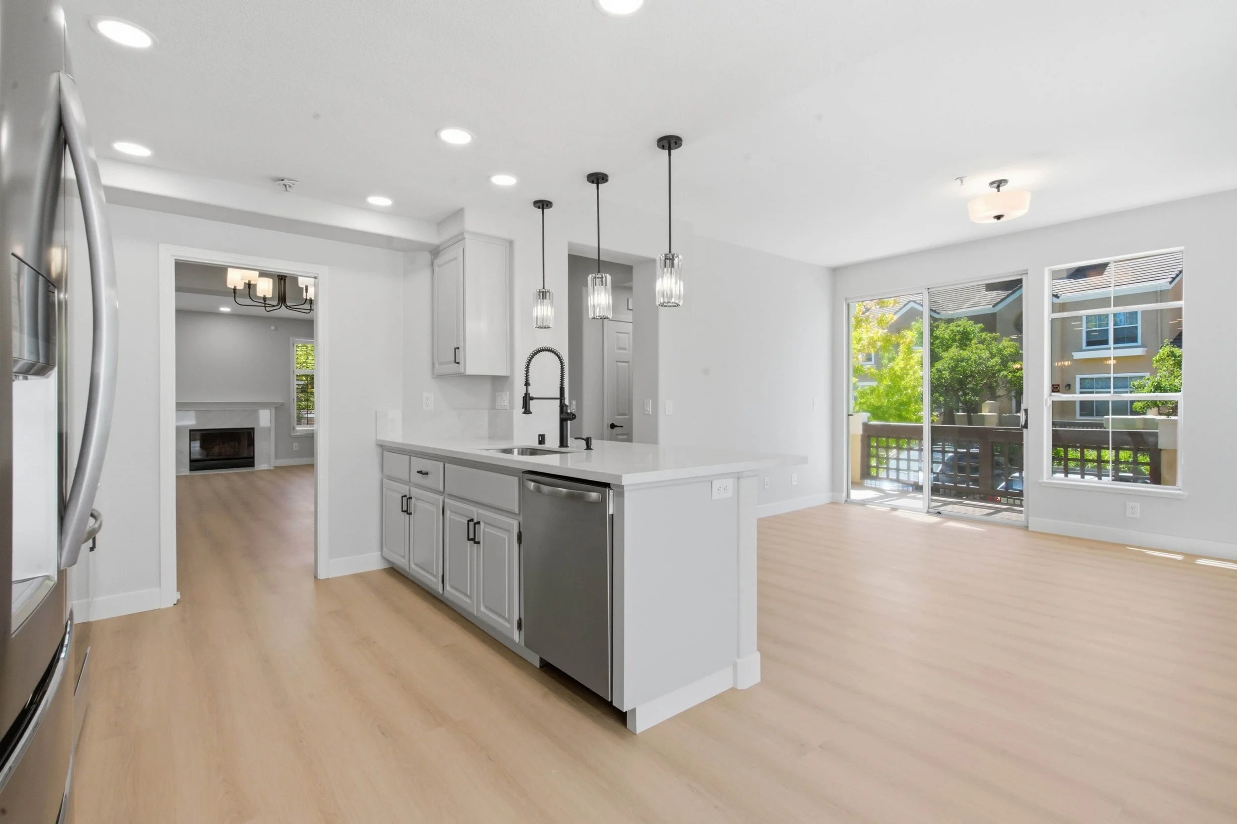 South Bay renovated condominium kitchen and dining room. The kitchen island is the focal point with a view of glass sliding doors. On the left is a stainless steel refrigerator.