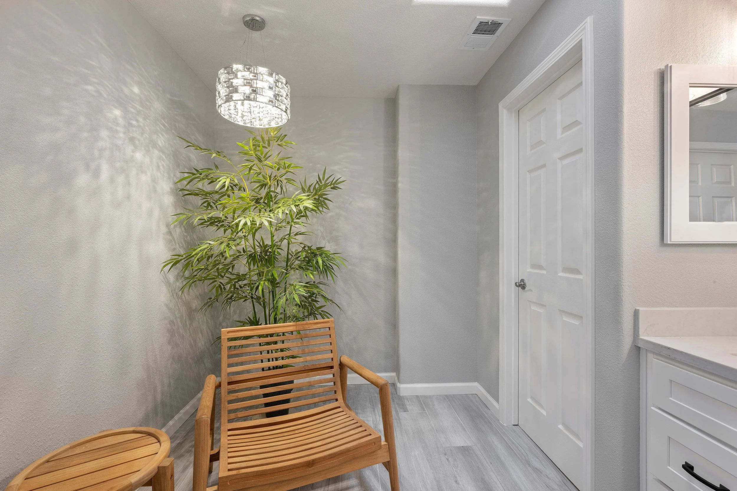 View of an entrance to a newly remodeled bathroom in San Jose. A teak chair is visible in the master bath, along with a chandelier. 