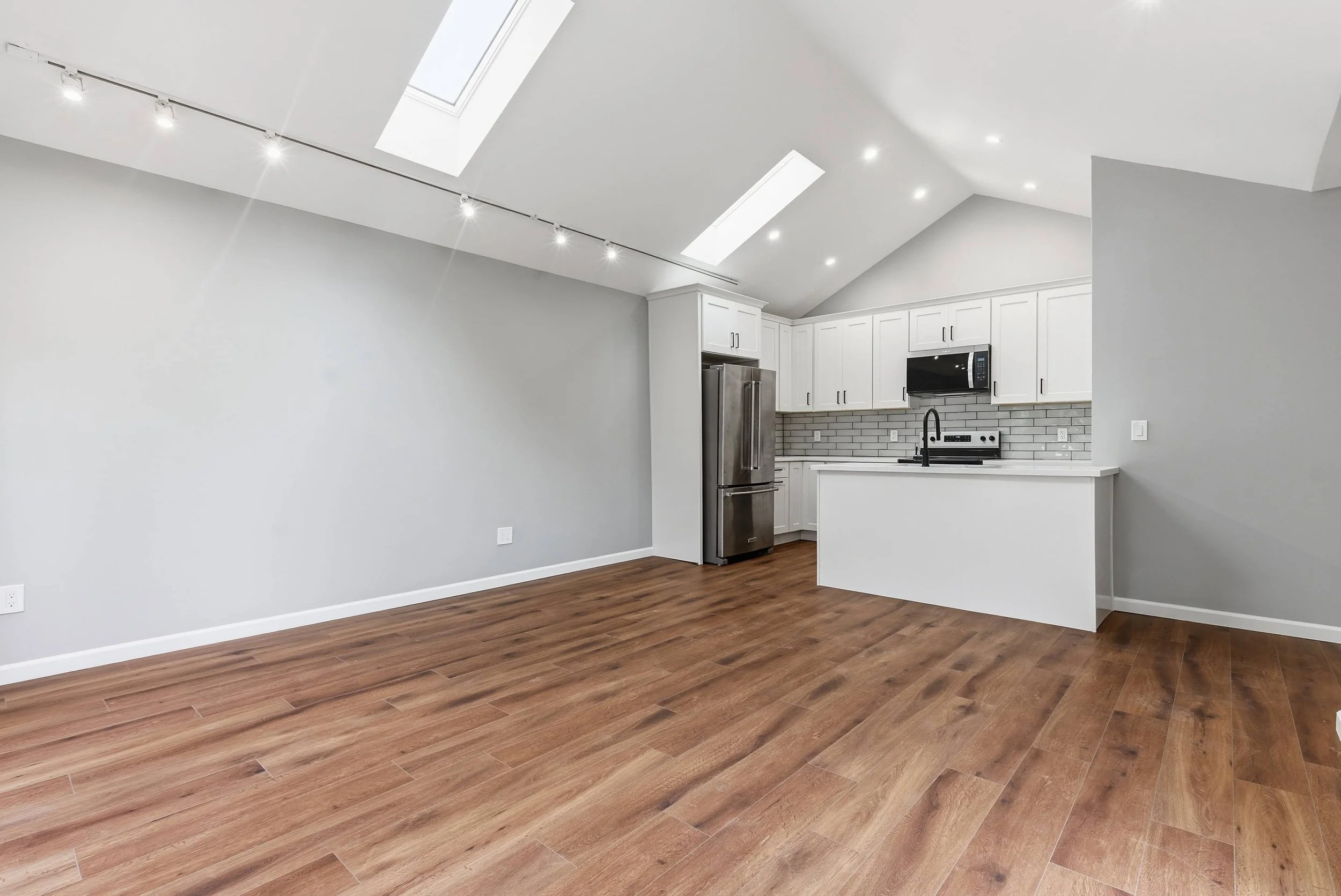 San Jose ADU with hardwood floors and gray walls. There are two skylights, track lighting, and the kitchen visible.