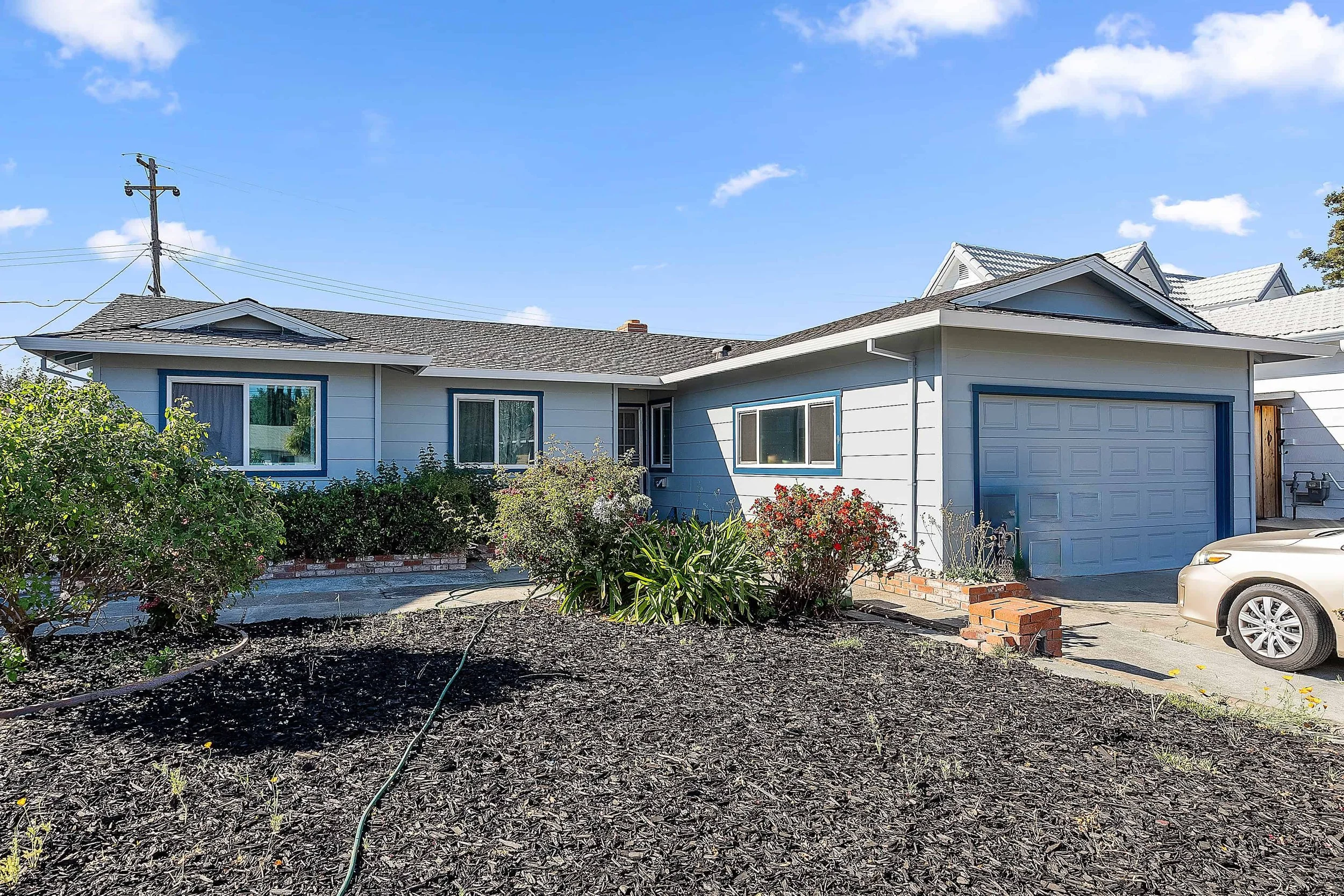 Light horizontally sided blue one story house with darker blue trim, street view with xeriscaped front yard.
