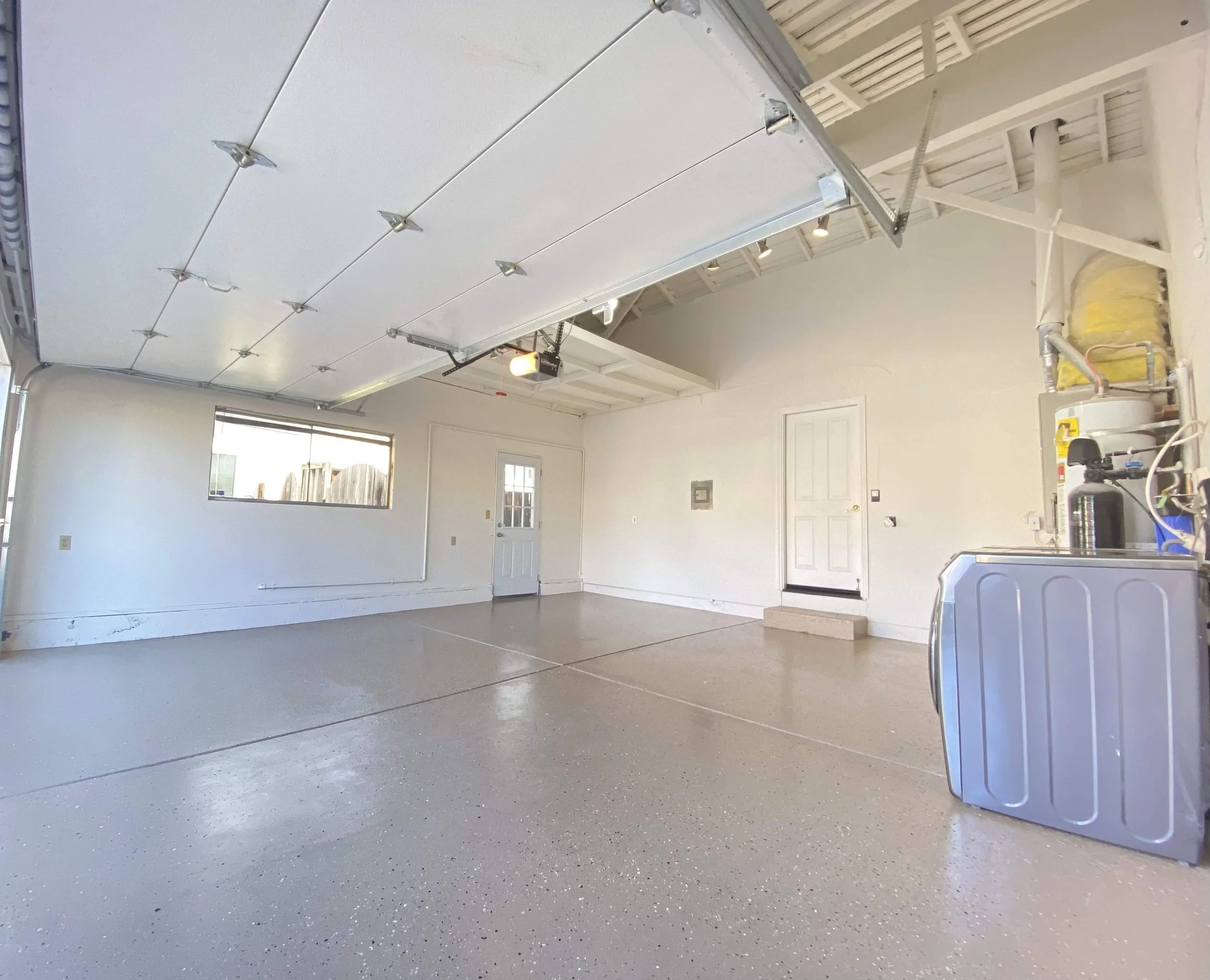 Empty garage with a concrete floor, a closed garage door, a window, a door leading outside, and some household items including a water heater and toolbox.