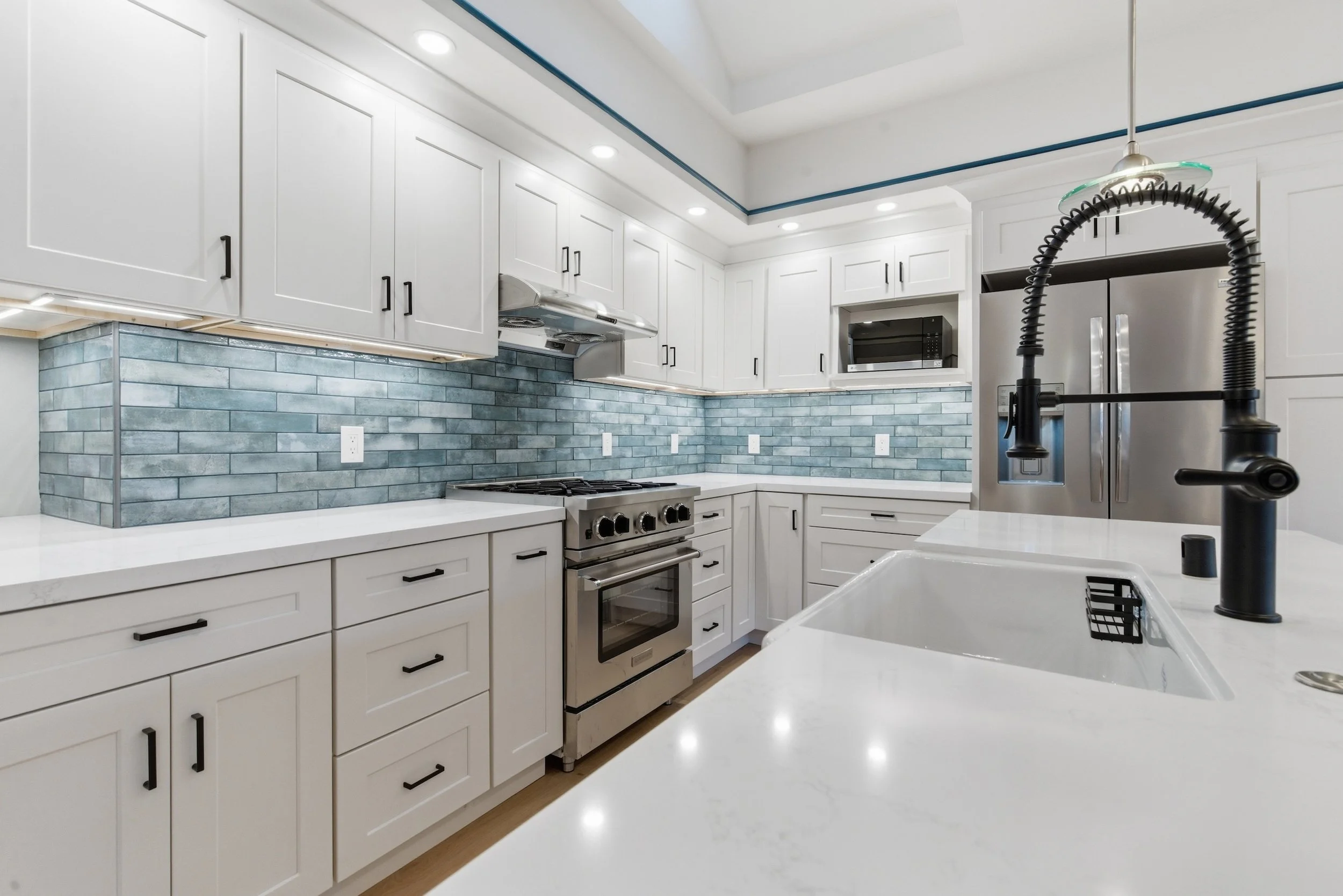 A modern kitchen with white cabinets, a blue tile backsplash, stainless steel appliances, a black gooseneck faucet, and a white countertop.