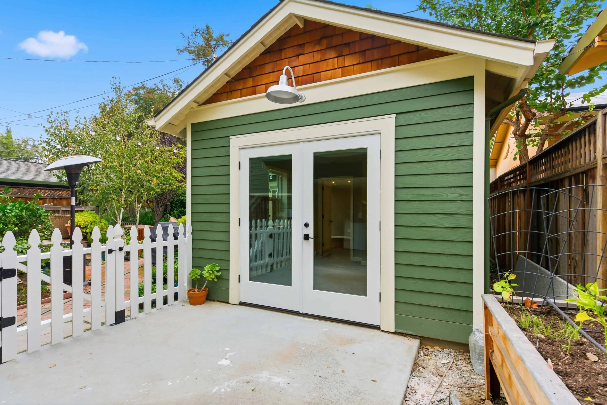 Naglee Park, San Jose new ADU with green horizontal siding and white French doors. Above the doors are cedar shingles and an outdoor wall sconce lighting fixture.