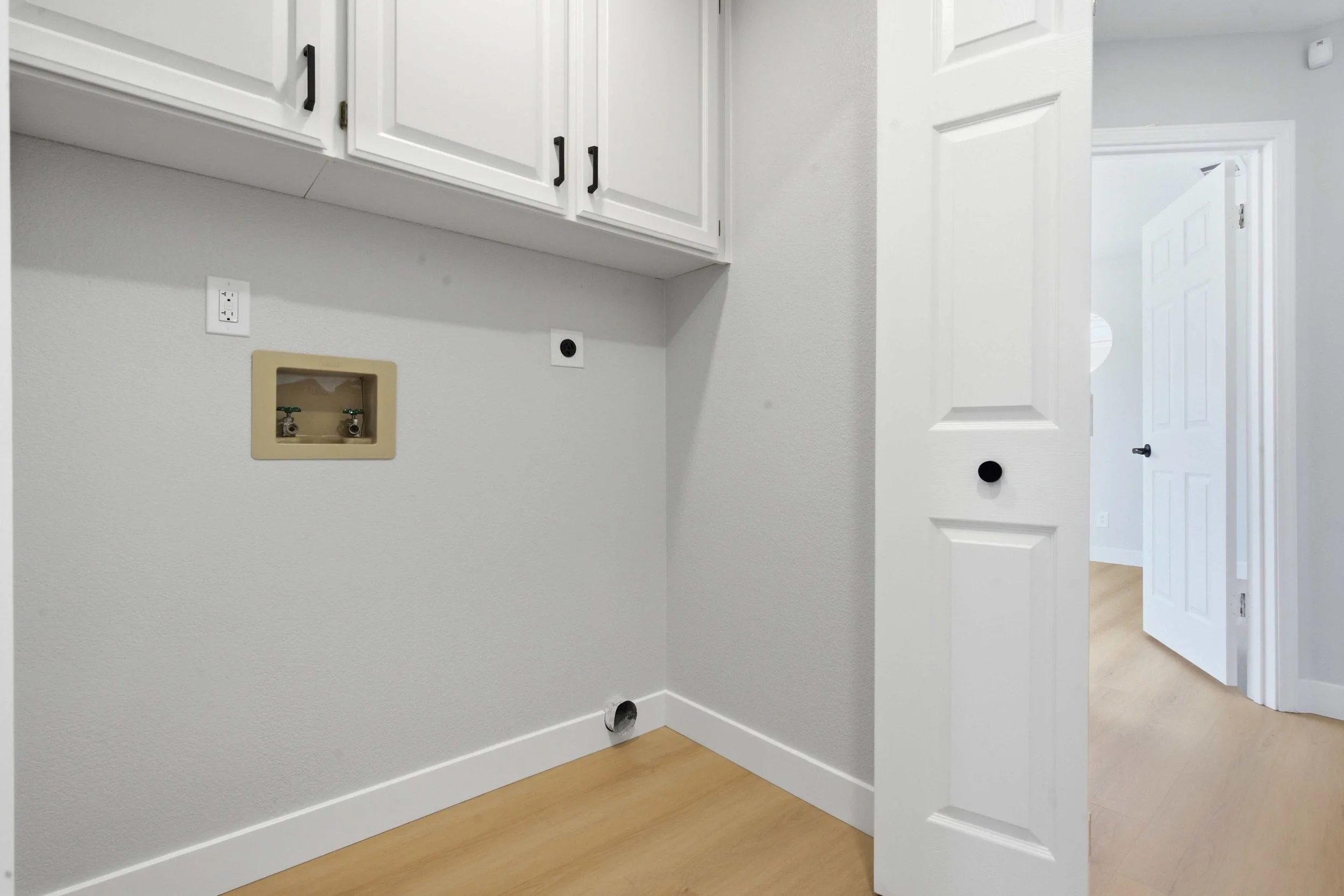 Renovated condo laundry room with hookups and new upper cabinets. The walls are gray and there are no appliances.