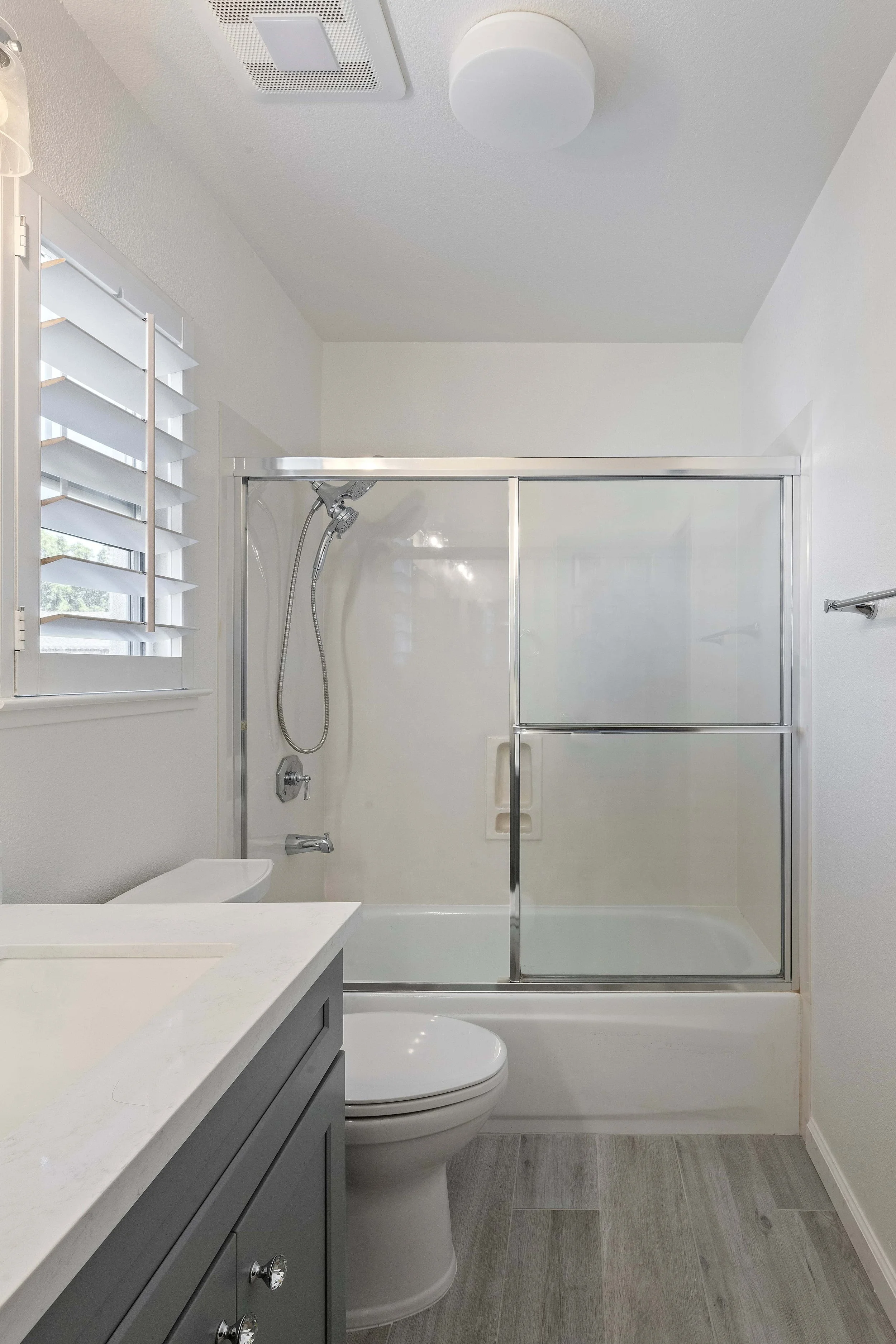 A remodeled San Jose bathroom. The grey plank floors are visible, as is the corner of the vanity, which is grey. The tub and shower are in the background.