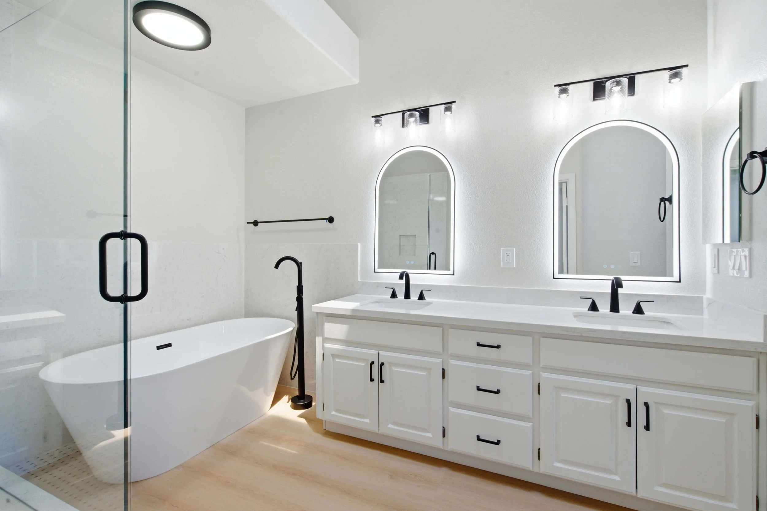 Double vanity with new countertops, lighting, and mirrors. To the left is a new soaking tub and ceiling light. This part of a larger renovation of a Bay Area condominium.