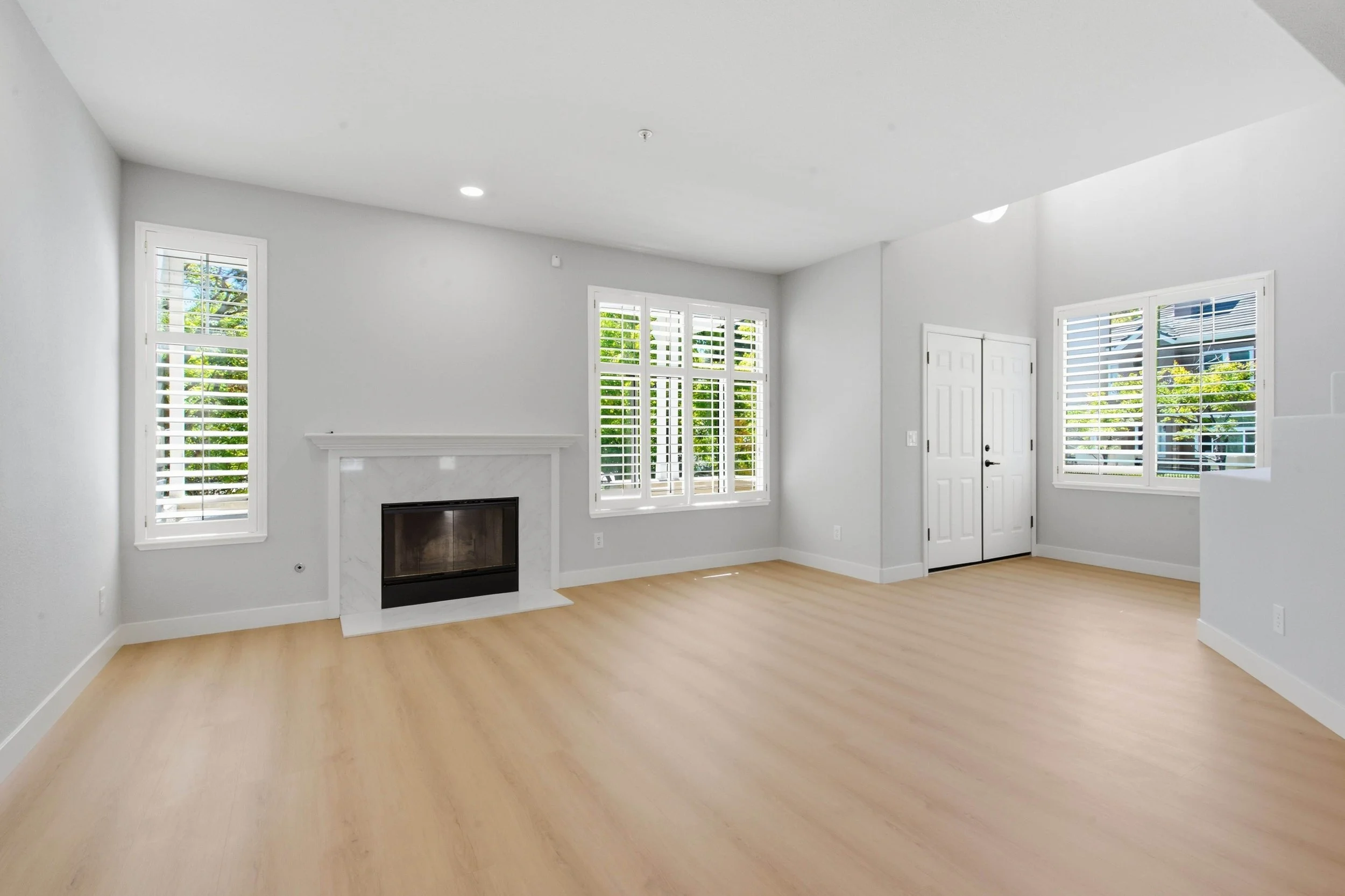 South Bay condo's Interior living room with a fireplace. The room has windows on two gray walls and wood floors.